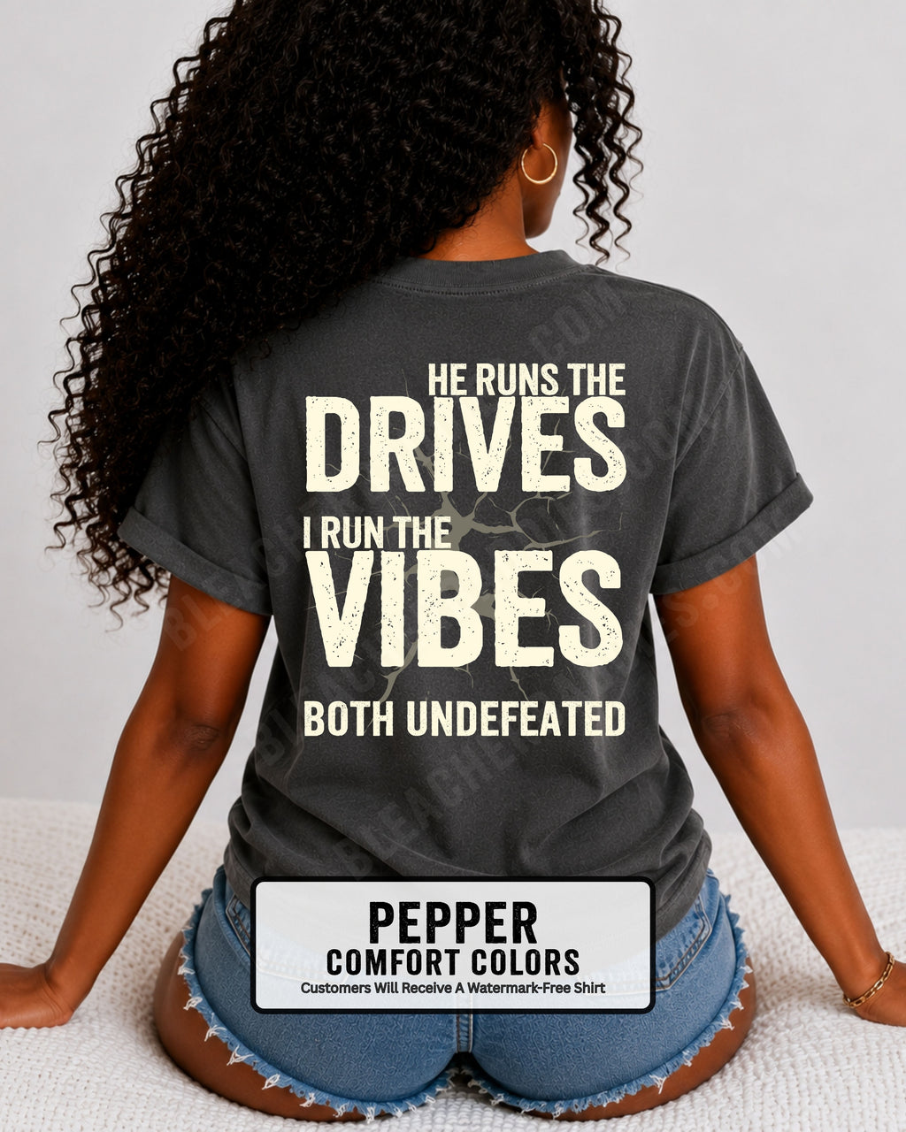 Woman wearing a pepper Comfort Colors football mom shirt from the back featuring the phrase "He Runs the Drives I Run the Vibes Both Undefeated" in distressed Typography with a cracked background graphic. Running back mom shirt. Quarterback mom shirt Football mom shirt.