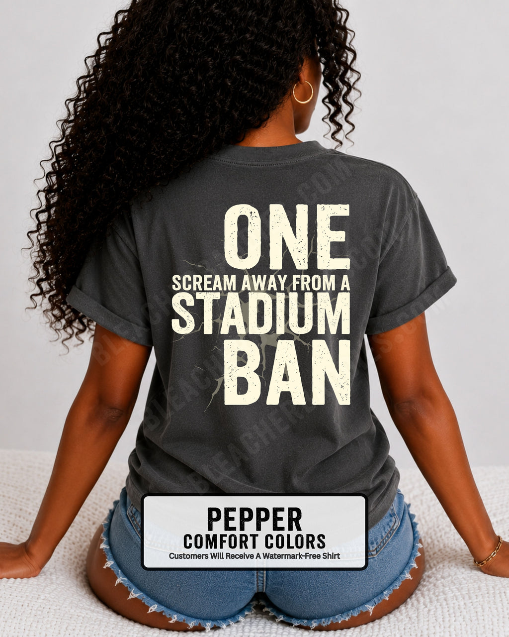 Woman wearing a pepper comfort colors t-shirt with a large distressed cream back graphic that reads “One Scream Away From a Stadium Ban” with a cracked texture effect across the design. Football mom shirt. Loud sports mom shirt.