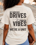 Woman standing in stadium stands wearing an ivory oversized t-shirt with a large distressed black back graphic that reads “He Wrecks Drives I Wreck Vibes We’re a Unit.” Football Mom Shirt. Defensive Lineman End Mom Shirt. Linebacker Mom Shirt. 