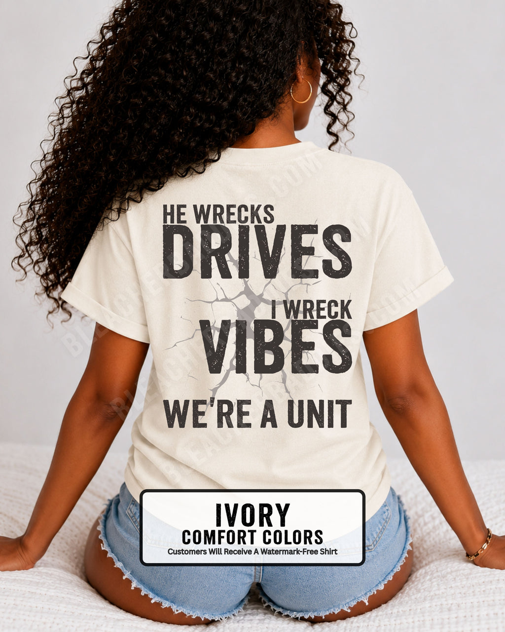 Woman wearing an ivory Comfort Colors t-shirt shown from the back featuring a large distressed black graphic that reads “He Wrecks Drives I Wreck Vibes We’re a Unit.” Football Mom Shirt