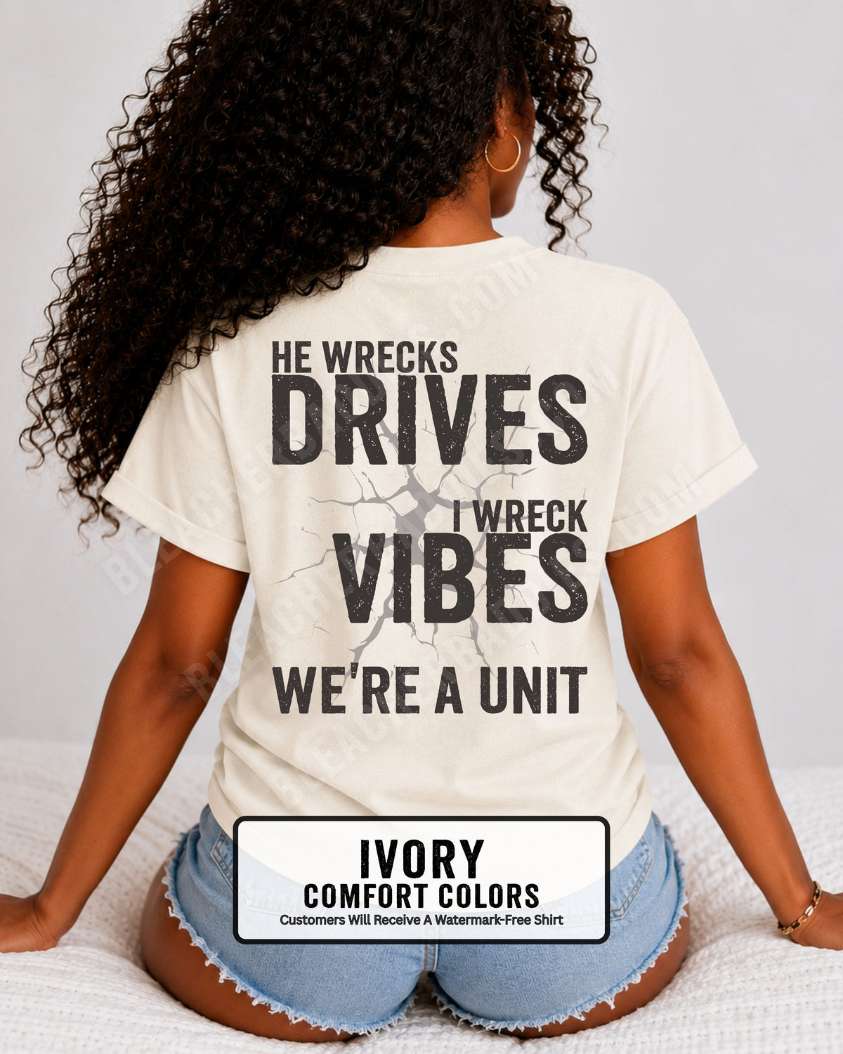 Woman wearing an ivory Comfort Colors t-shirt shown from the back featuring a large distressed black graphic that reads “He Wrecks Drives I Wreck Vibes We’re a Unit.” Football Mom Shirt