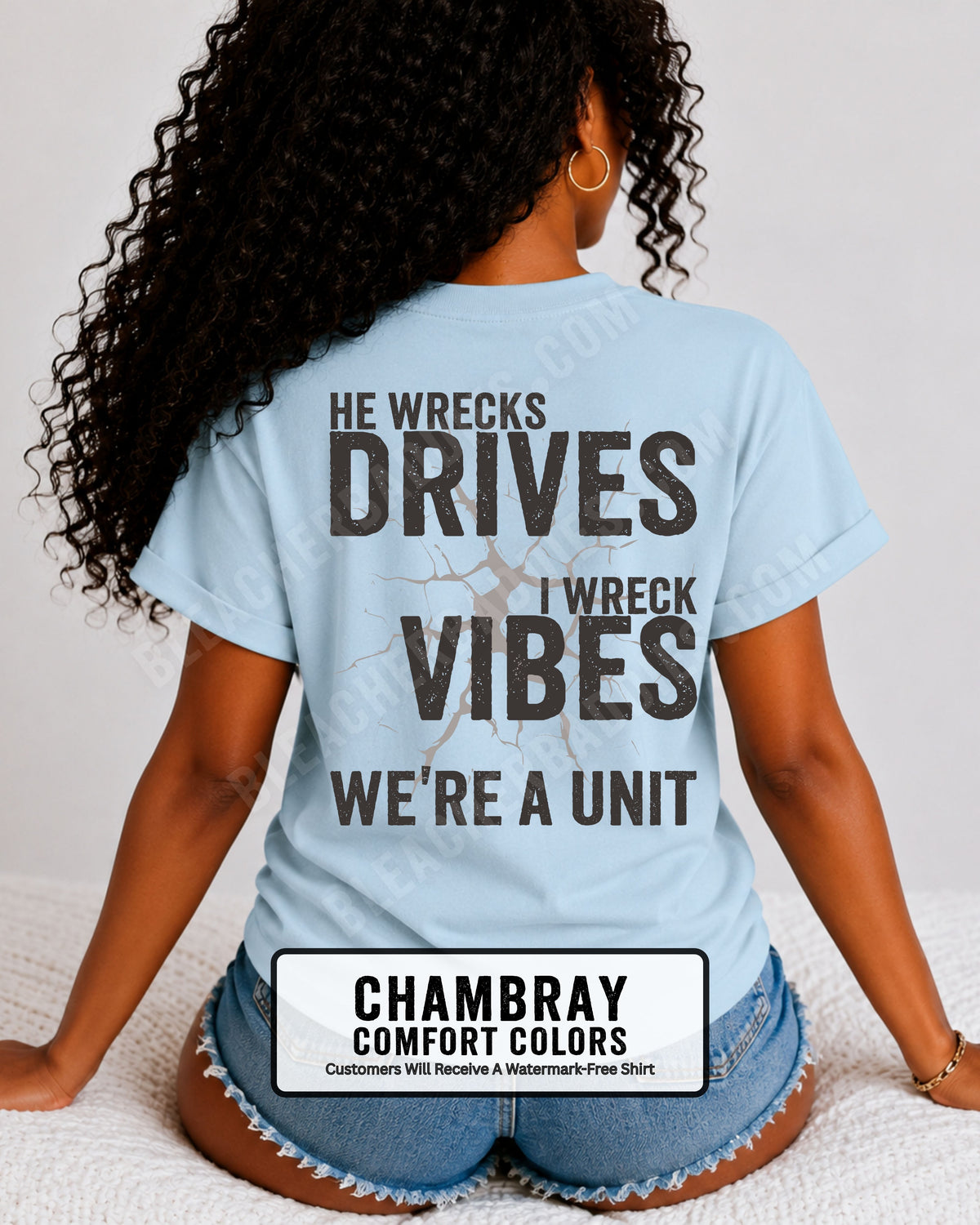 Woman wearing a chambray blue Comfort Colors t-shirt shown from the back featuring a large distressed black graphic that reads “He Wrecks Drives I Wreck Vibes We’re a Unit.” Football Mom Shirt