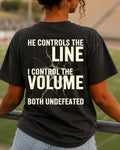 Back view of woman wearing black Comfort Colors football mom game day shirt in stadium featuring “He Controls the Line I Control the Volume Both Undefeated” bold graphic design
