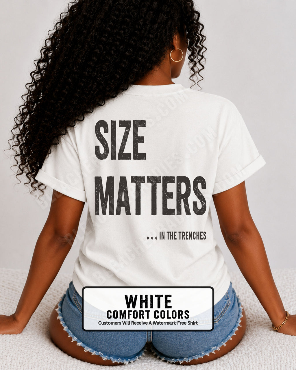 Back view of a woman wearing a WHITE Comfort Colors t-shirt with an oversized distressed graphic reading "Size Matters... In the Trenches." Casual football fan shirt styled with denim shorts in a bright lifestyle setting.