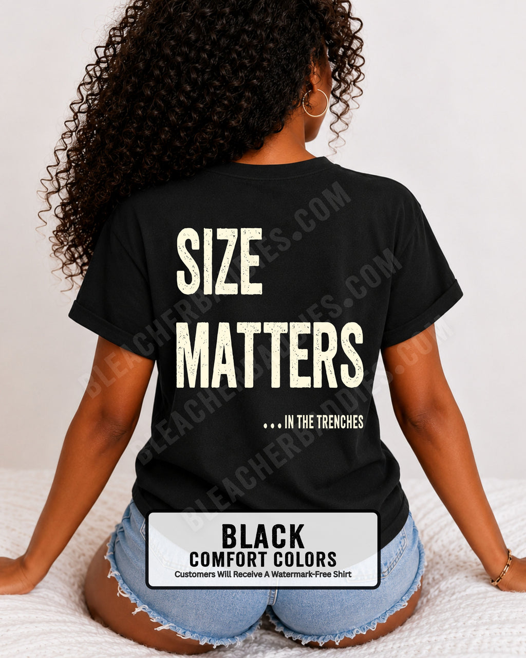 Back view of a woman wearing a BLACK  Comfort Colors t-shirt with an oversized distressed graphic reading "Size Matters... In the Trenches." Casual football fan shirt styled with denim shorts in a bright lifestyle setting.