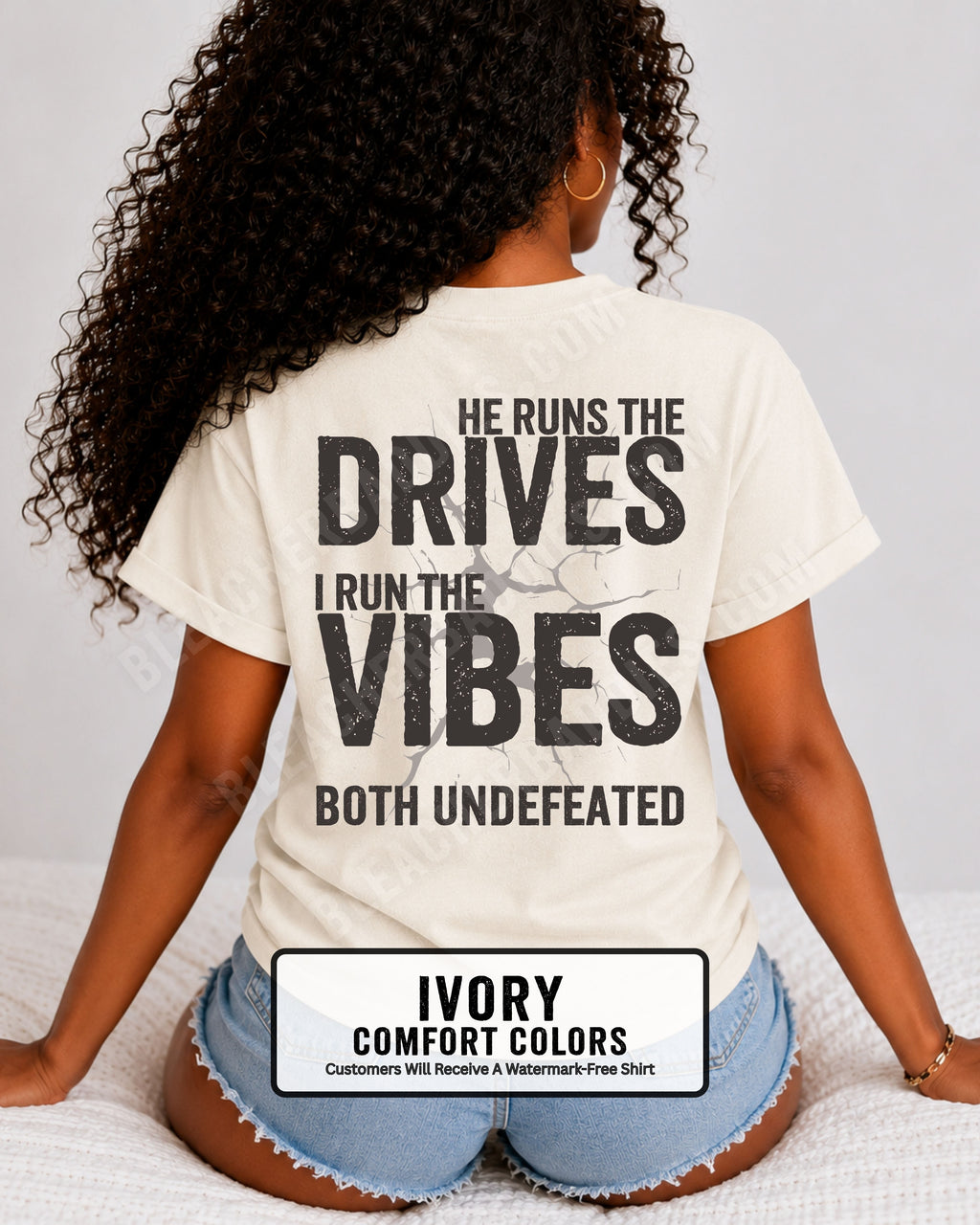 Woman wearing an ivory Comfort Colors football mom shirt from the back featuring the phrase "He Runs the Drives I Run the Vibes Both Undefeated" in distressed Typography with a cracked background graphic. Running back mom shirt. Quarterback mom shirt Football mom shirt.