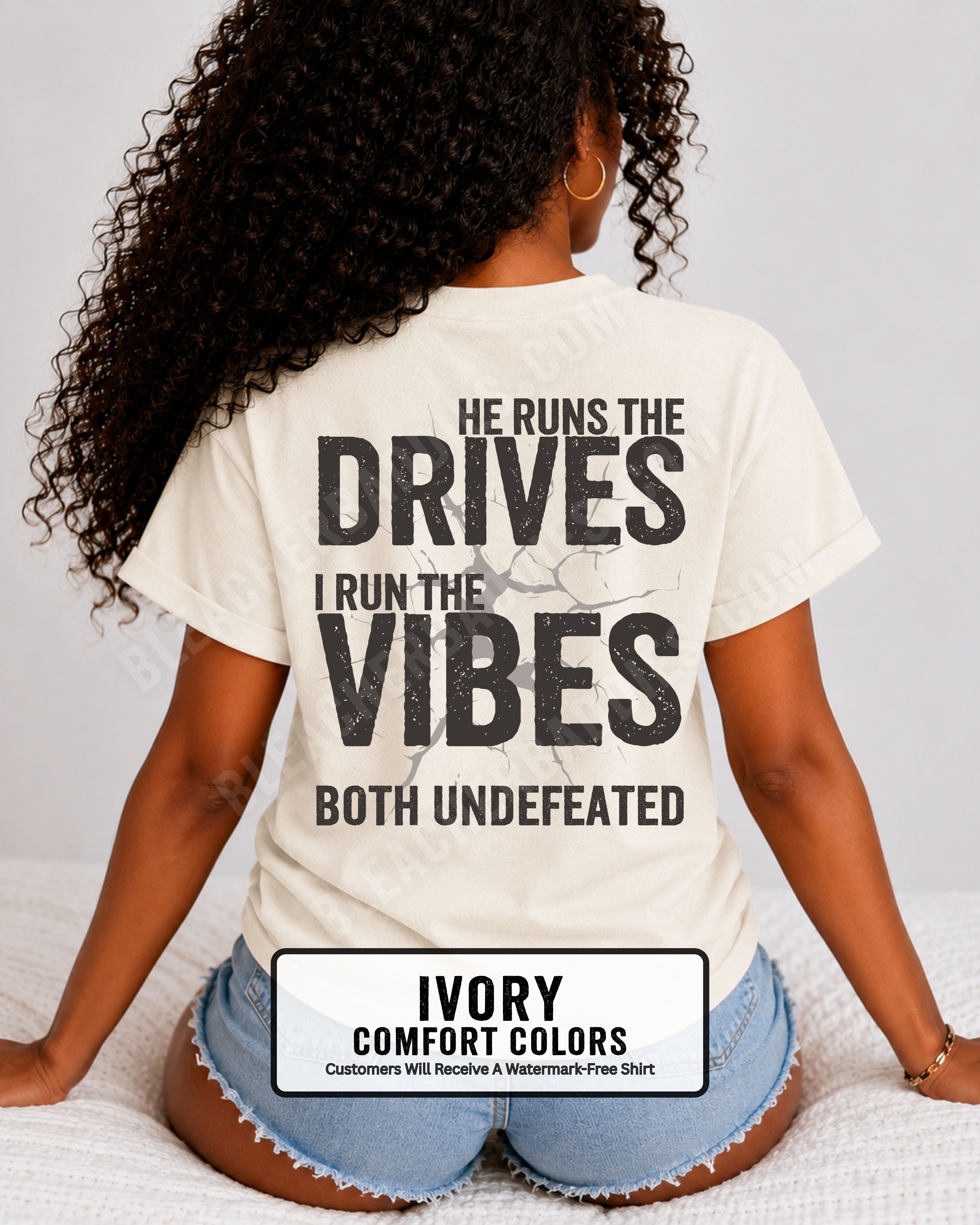 Woman wearing an ivory Comfort Colors football mom shirt from the back featuring the phrase "He Runs the Drives I Run the Vibes Both Undefeated" in distressed Typography with a cracked background graphic. Running back mom shirt. Quarterback mom shirt Football mom shirt.