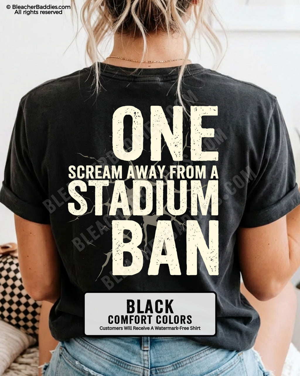 Woman wearing a black  t-shirt with a large distressed cream back graphic that reads “One Scream Away From a Stadium Ban” with a cracked texture effect across the design.