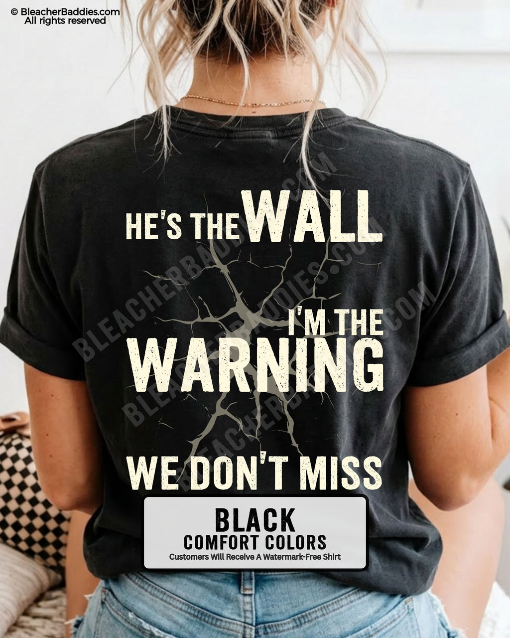 Woman wearing a black football mom game day shirt shown from the back featuring a large distressed cream graphic that reads “He’s the Wall I’m the Warning We Don’t Miss.”
