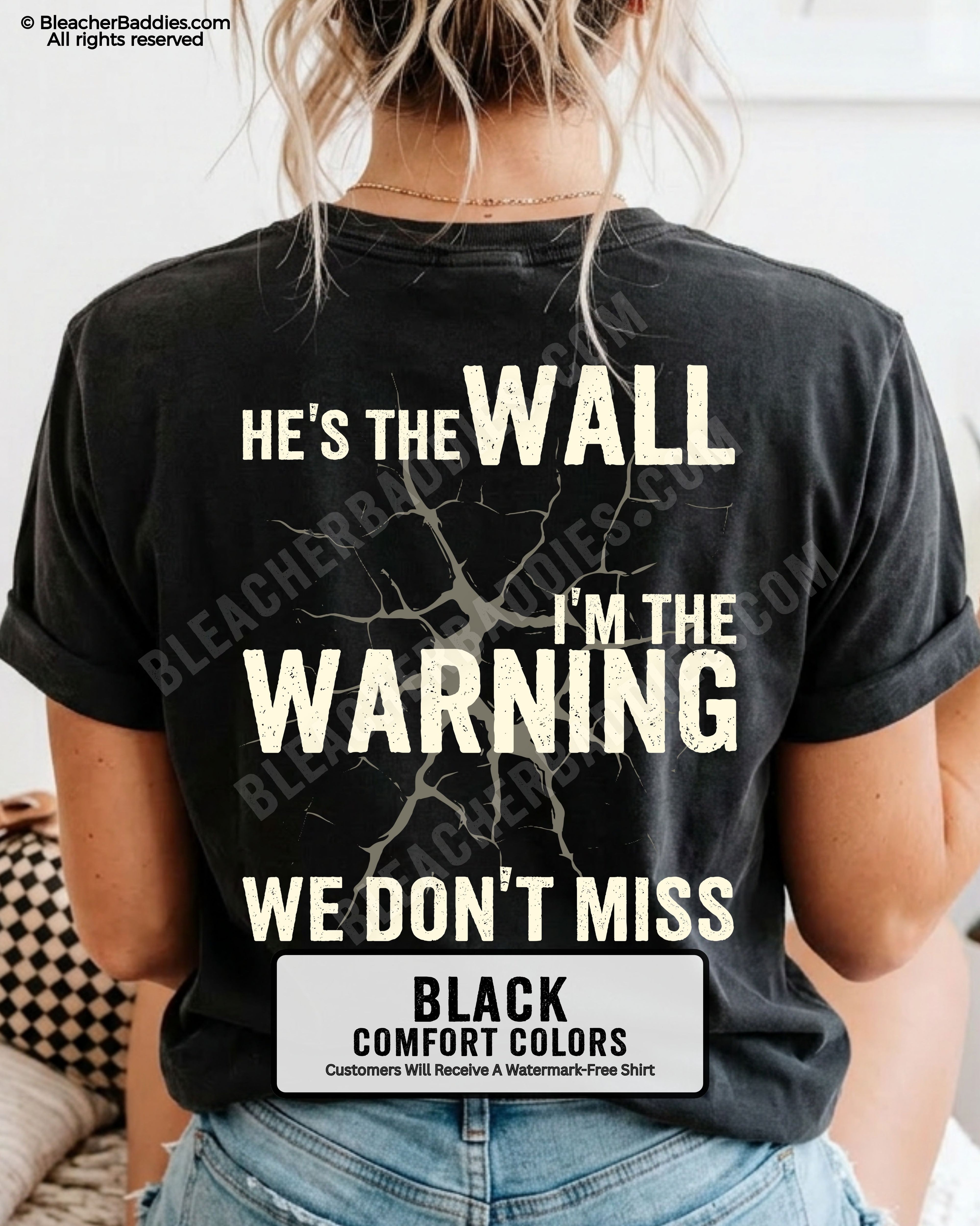 Woman wearing a black football mom game day shirt shown from the back featuring a large distressed cream graphic that reads “He’s the Wall I’m the Warning We Don’t Miss.”