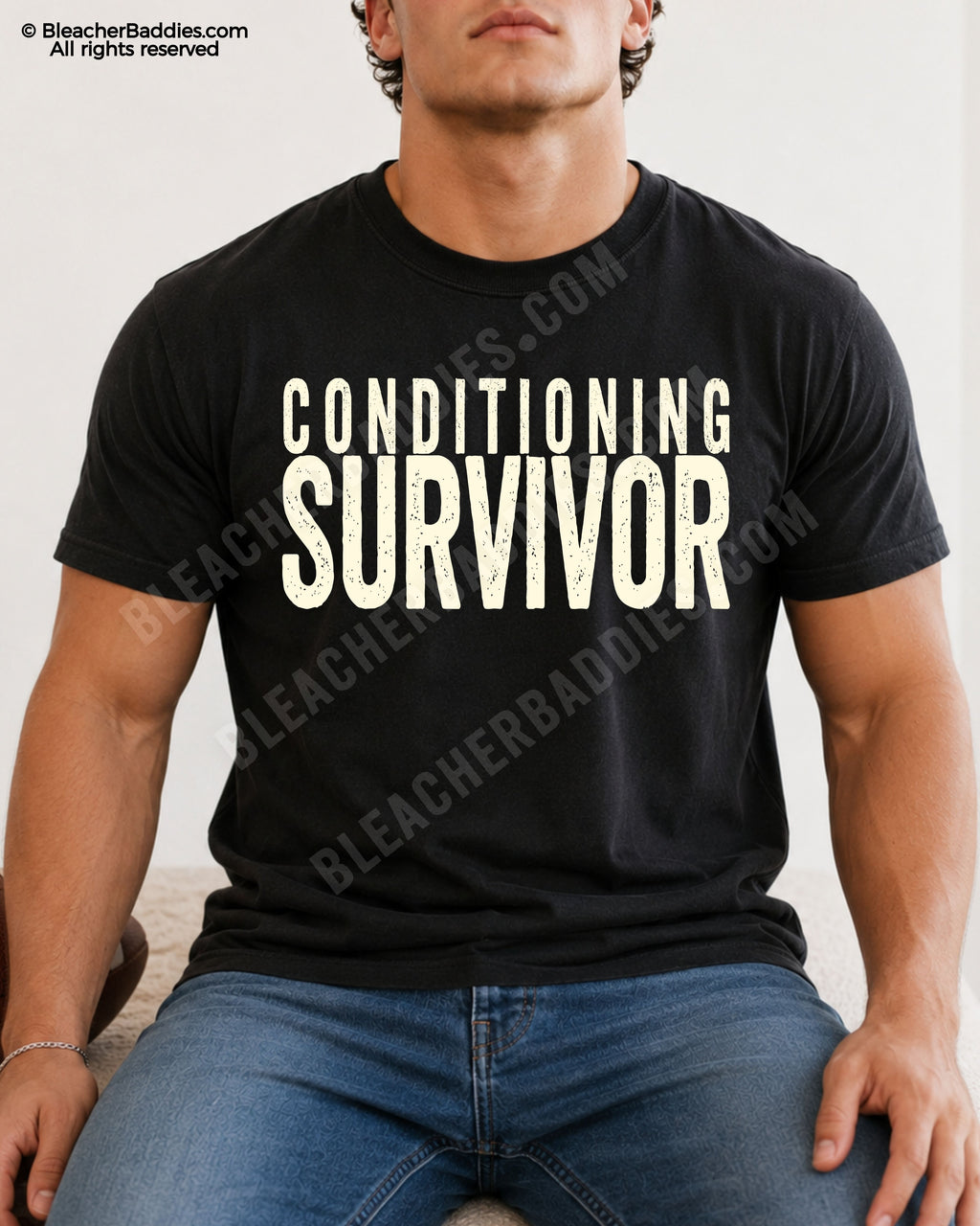 Male football player model wearing a black Comfort Colors “Conditioning Survivor” football shirt with distressed black typography while seated indoors in casual denim jeans.
