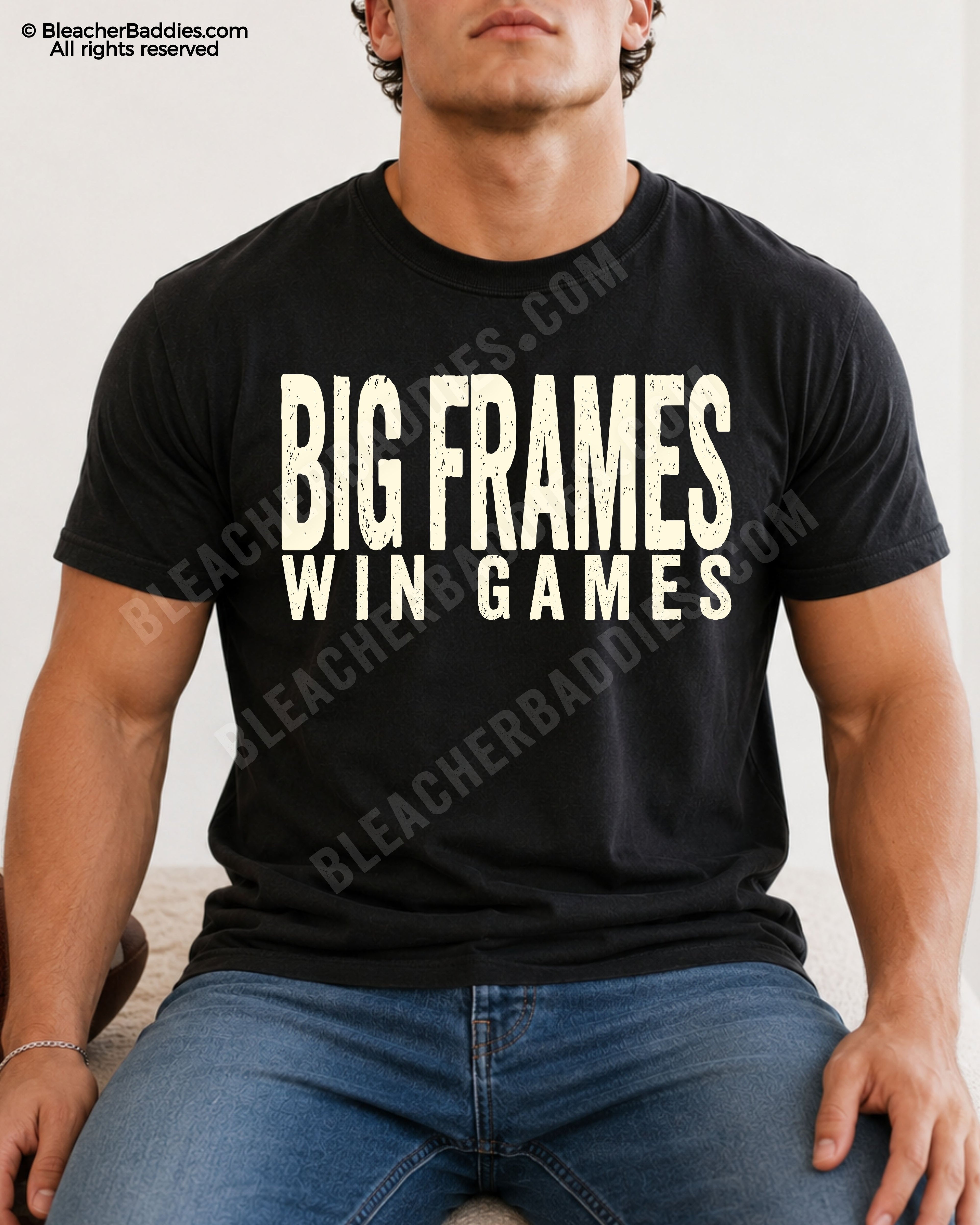 Male football player model wearing a BLACK Comfort Colors “Big Frames Win Games” football shirt with distressed CREAM typography while seated indoors in jeans.
