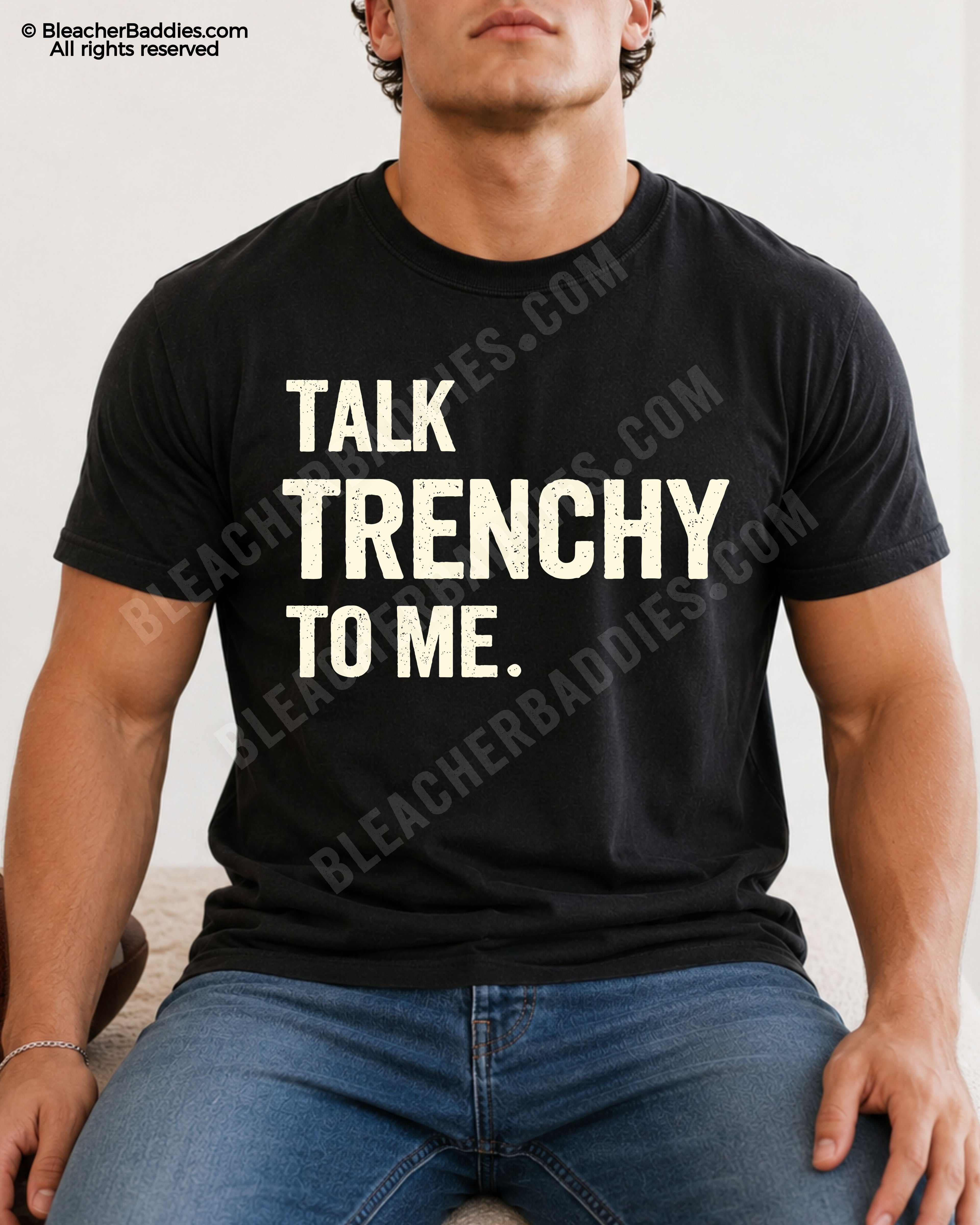 Athletic male model sitting while wearing a black Comfort Colors 1717 t-shirt with "Talk Trenchy to Me" football lineman graphic and distressed blue jeans.