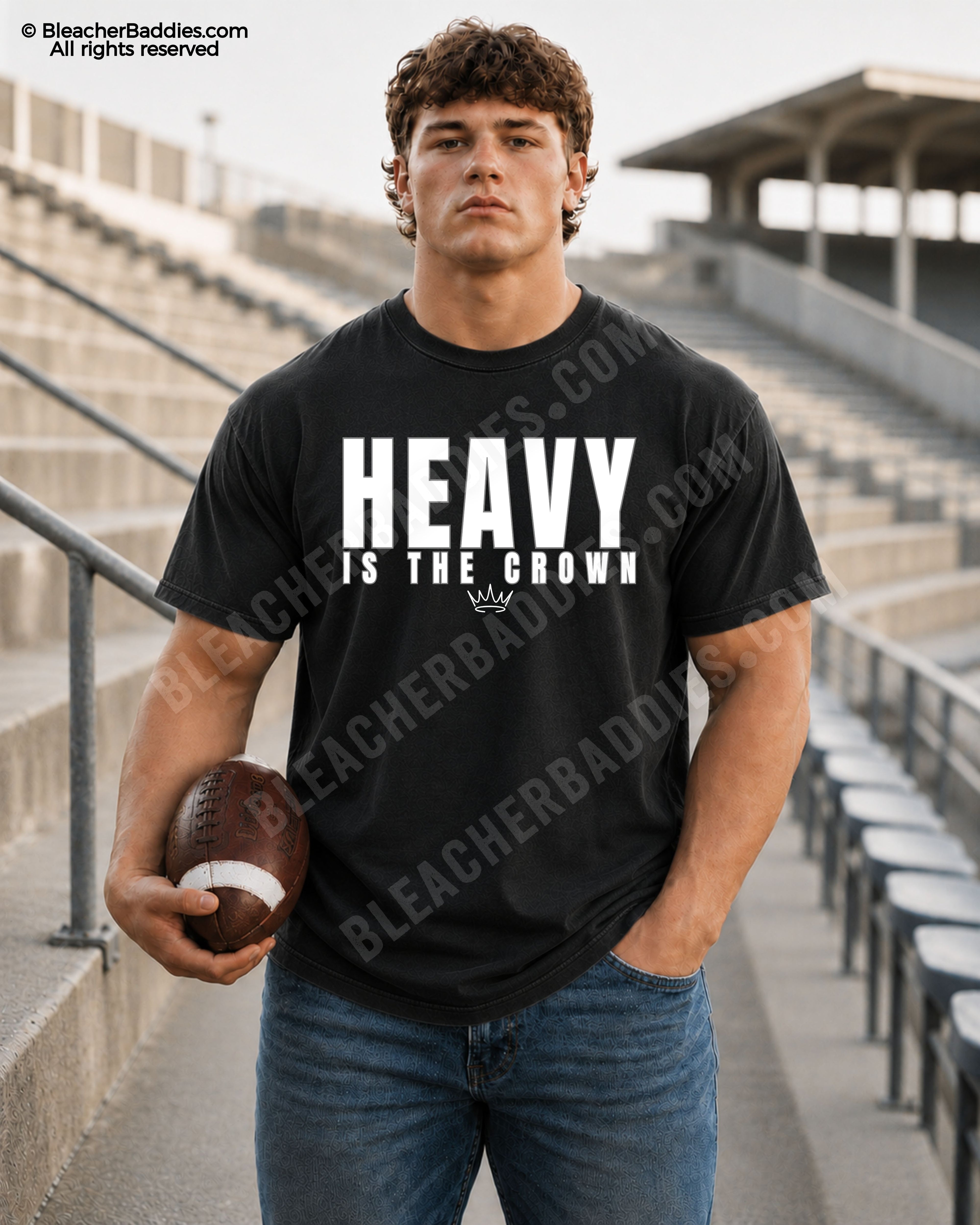 Football player standing in stadium bleachers wearing a black “HEAVY IS THE CROWN” athlete mindset graphic t-shirt while holding a football and wearing blue jeans.