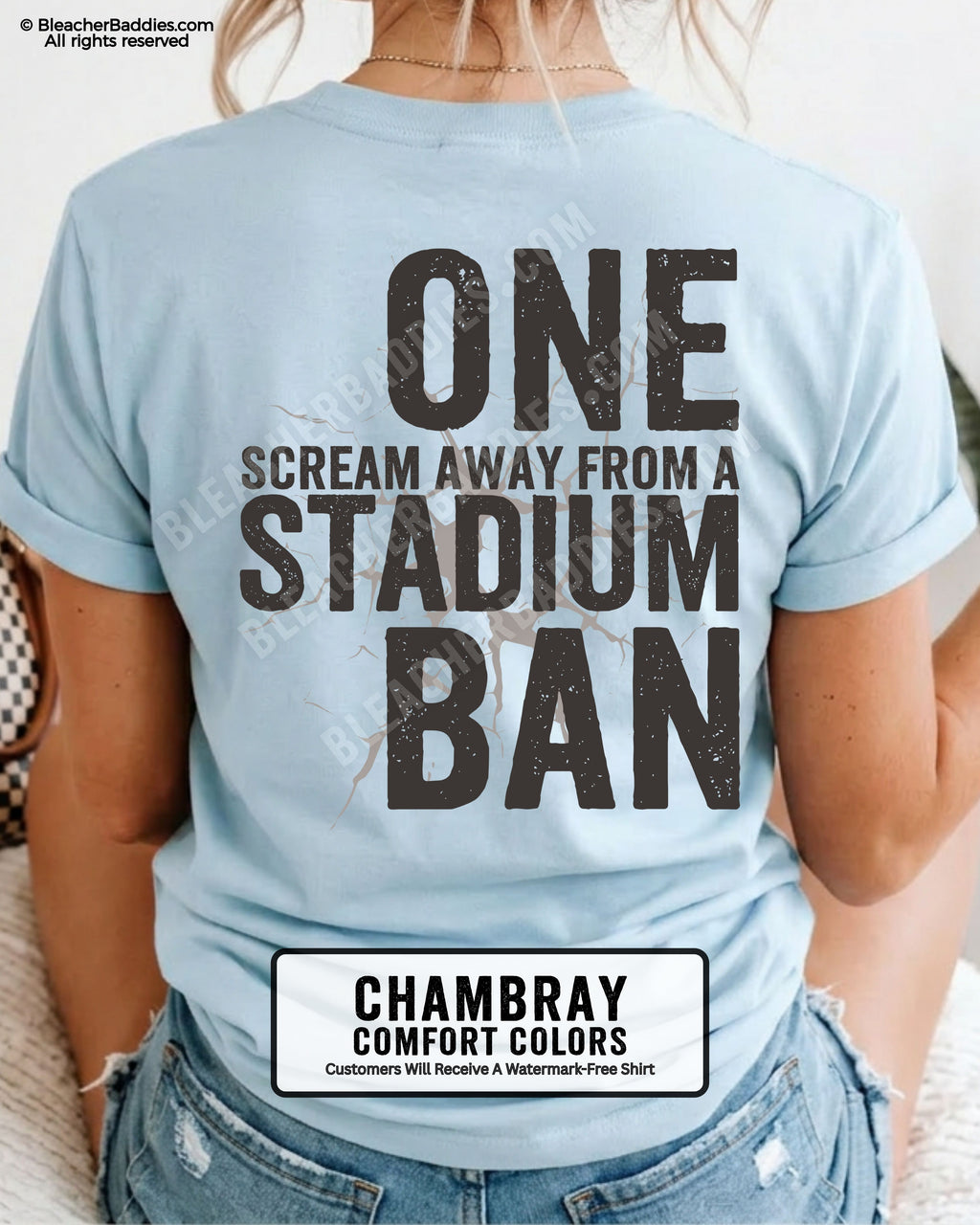 Woman wearing a chambray blue t-shirt with a large distressed black back graphic that reads “One Scream Away From a Stadium Ban” with a cracked texture effect across the design.