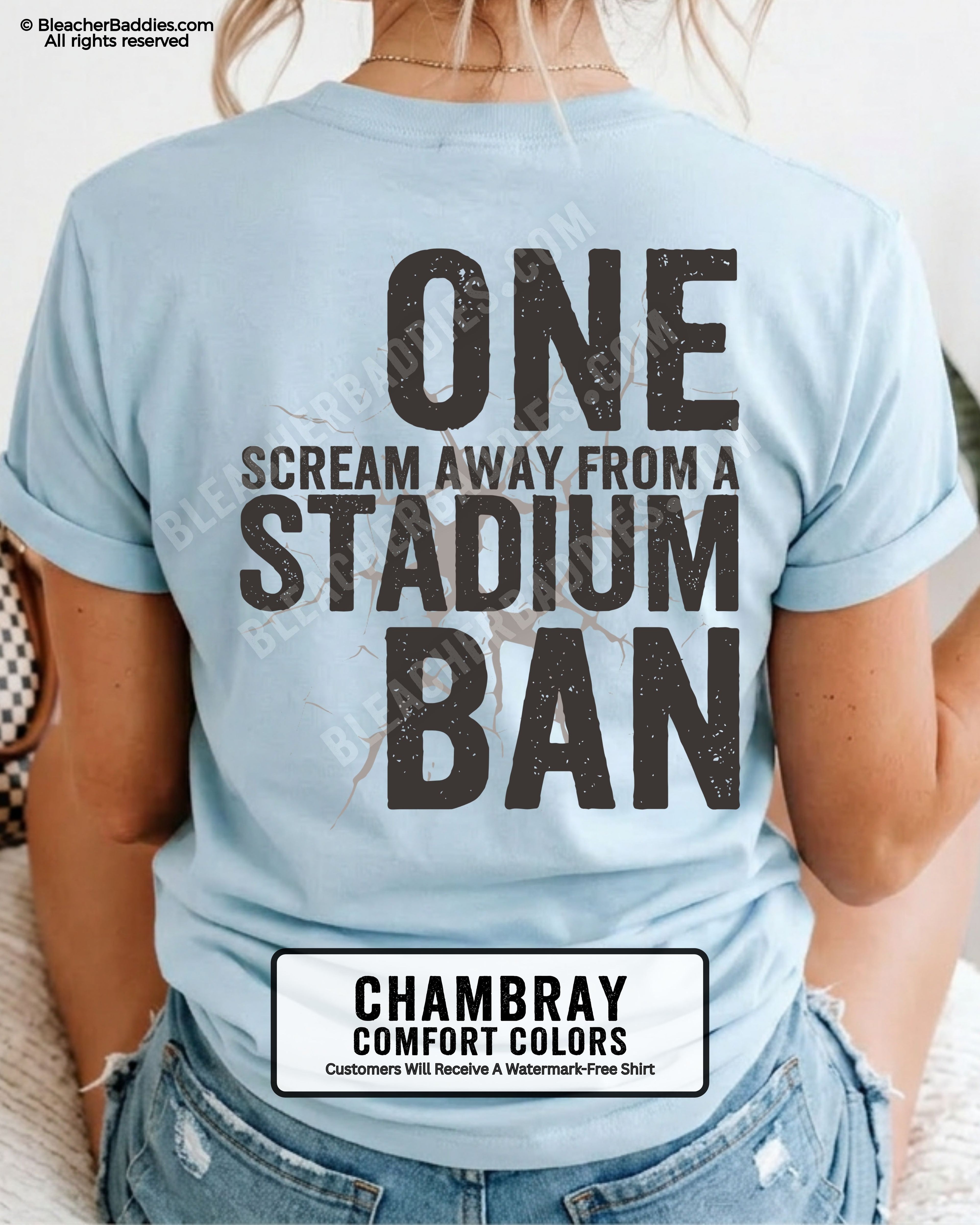 Woman wearing a chambray blue t-shirt with a large distressed black back graphic that reads “One Scream Away From a Stadium Ban” with a cracked texture effect across the design.