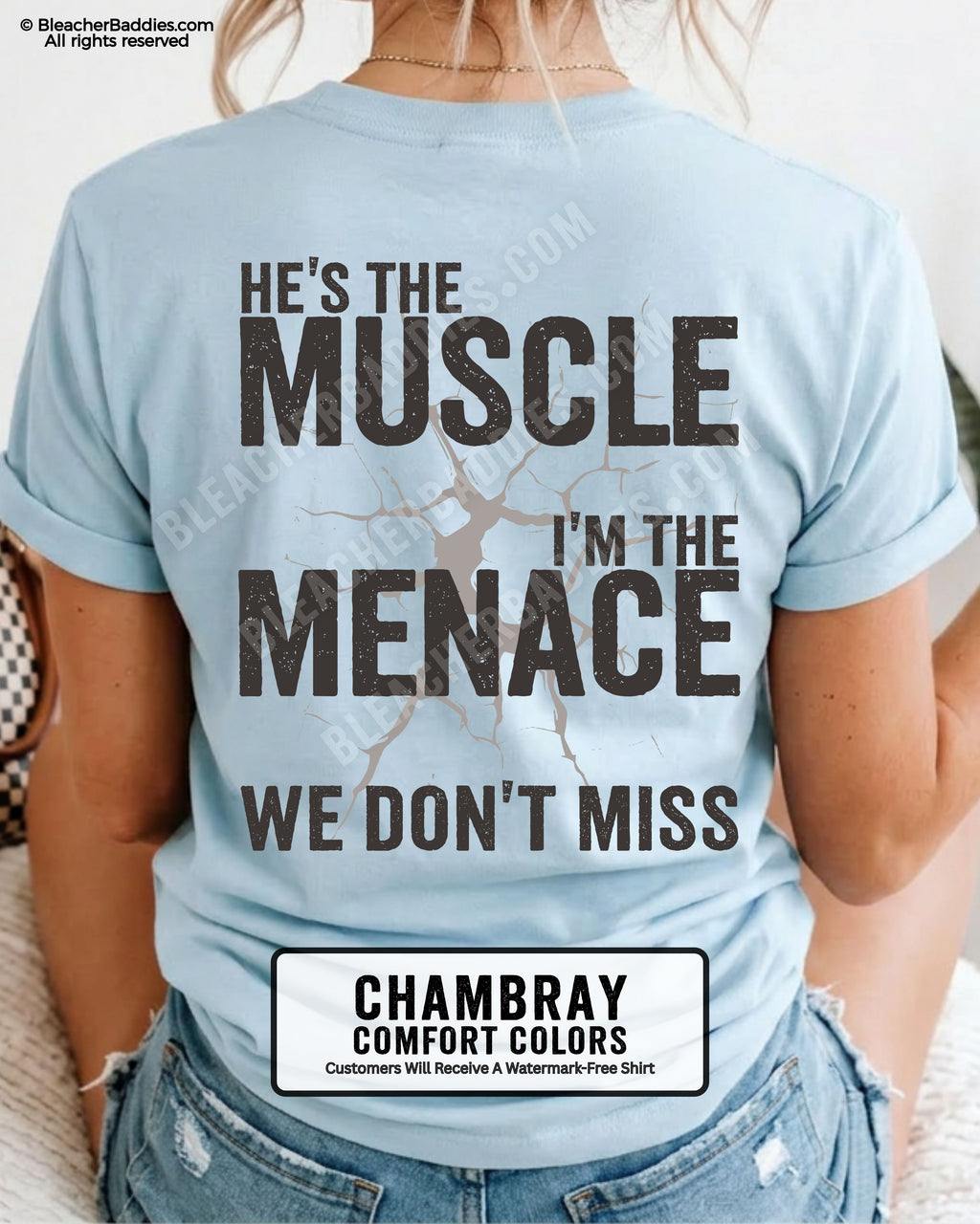Woman wearing chambray Comfort Colors football mom game day shirt with back design that reads “He’s the muscle I’m the menace we don’t miss” in distressed black text with cracked graphic and chambray color label shown