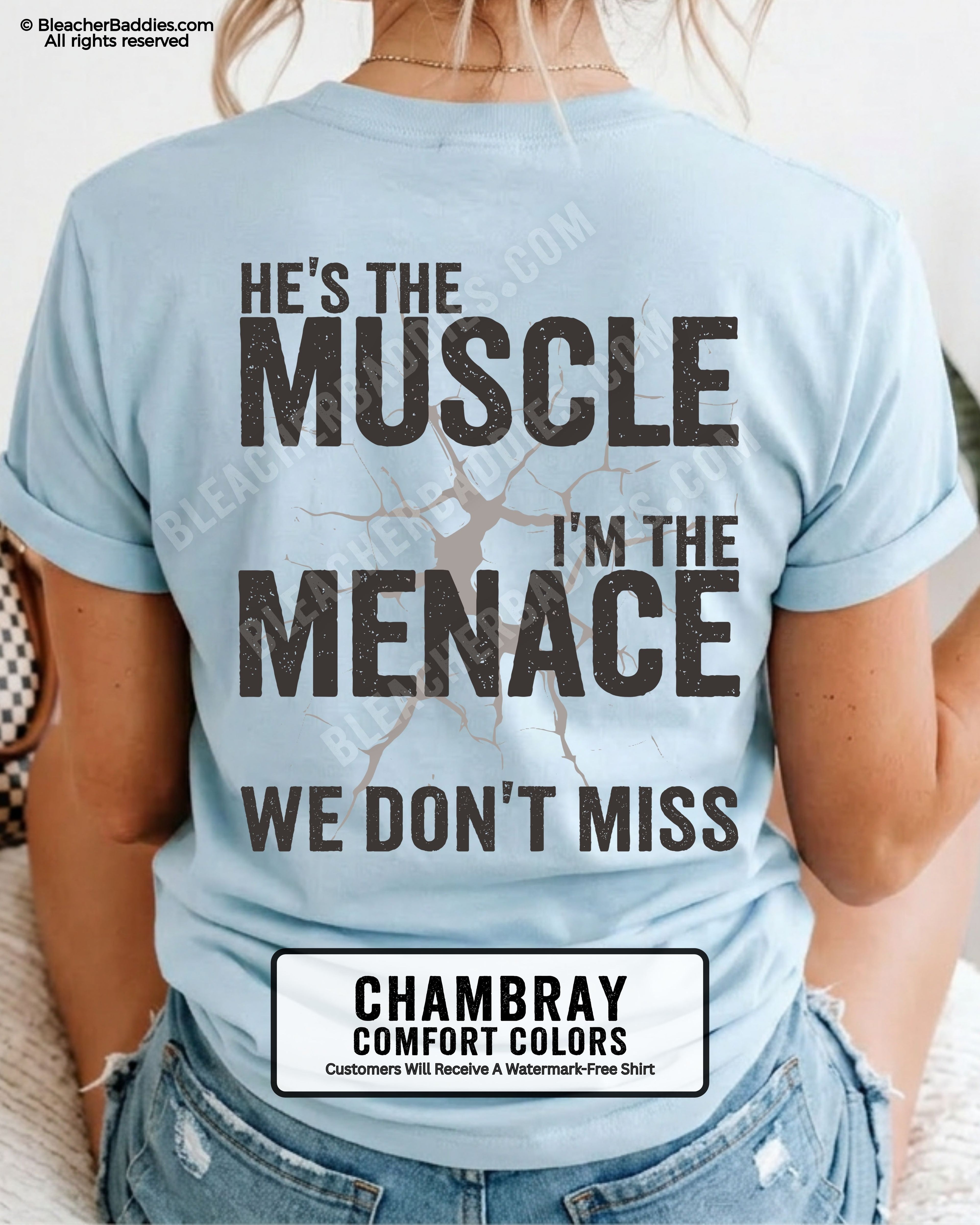 Woman wearing chambray Comfort Colors football mom game day shirt with back design that reads “He’s the muscle I’m the menace we don’t miss” in distressed black text with cracked graphic and chambray color label shown