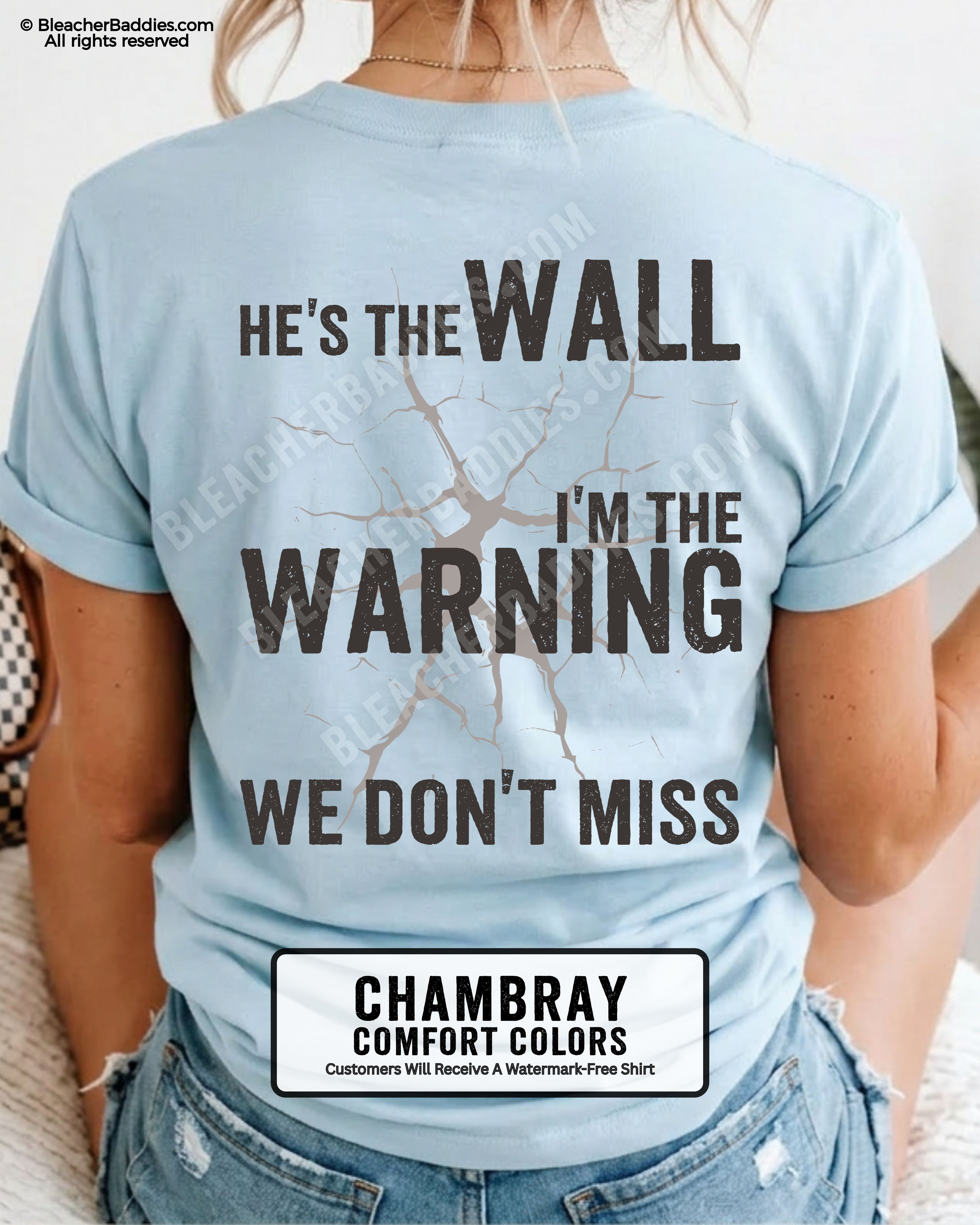 Woman wearing a chambray blue football mom game day shirt shown from the back featuring a large distressed black graphic that reads “He’s the Wall I’m the Warning We Don’t Miss.”