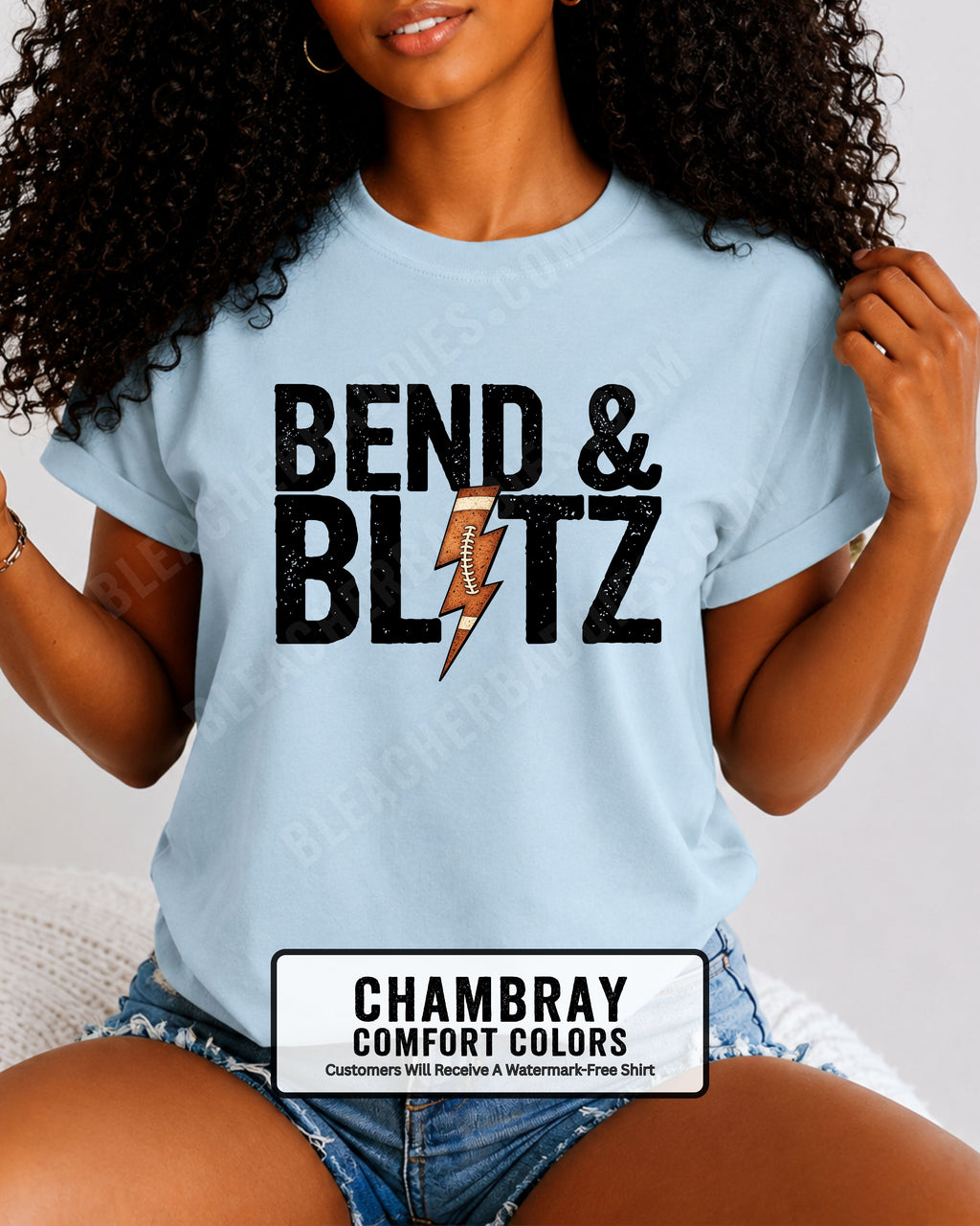 Close-up lifestyle photo of a football mom wearing a chambray Comfort Colors t-shirt with the distressed black graphic "BEND & BLITZ" and a football lightning bolt design between the words. 
