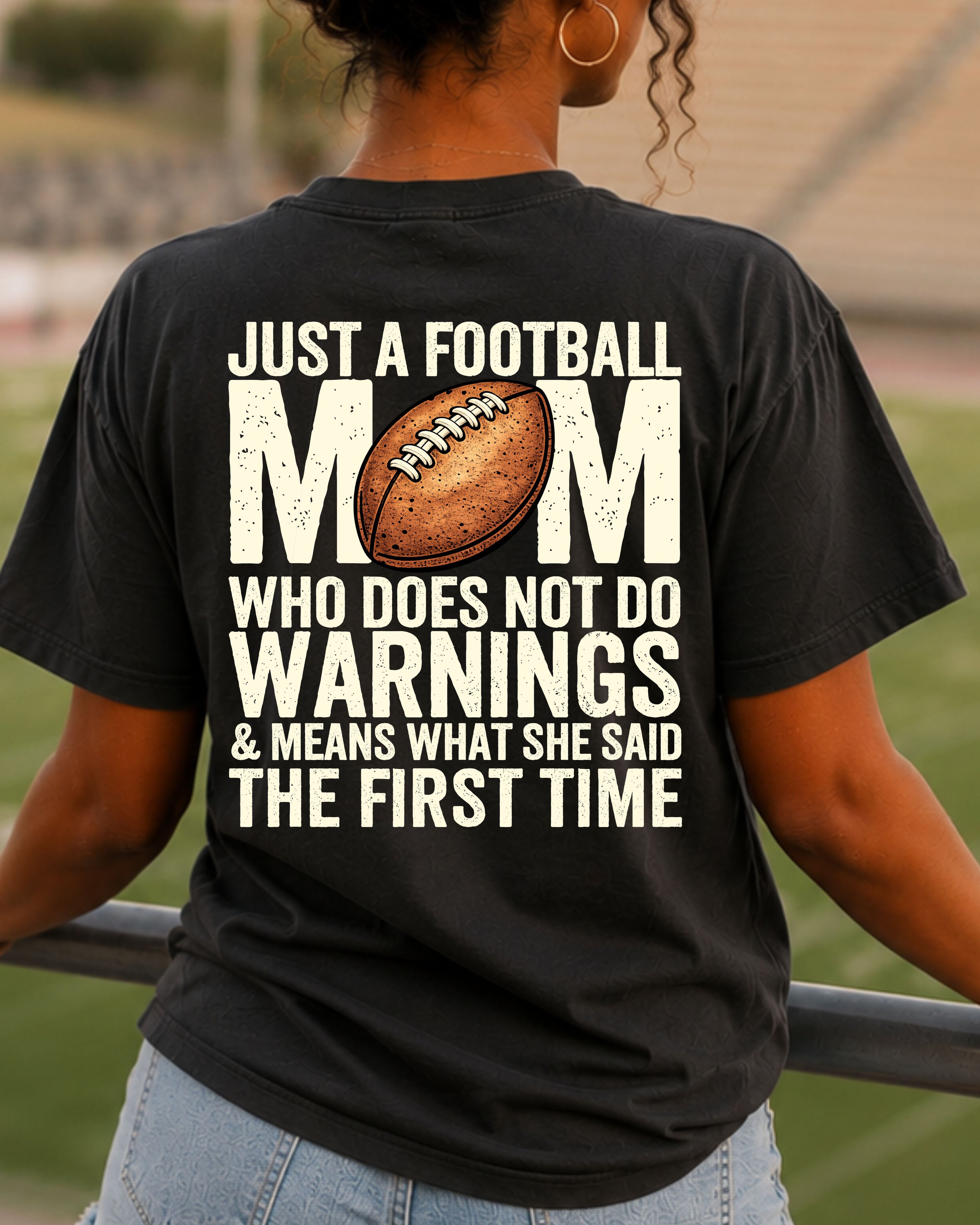 Football mom game day comfort colors black shirt worn in stadium stands with back graphic reading “Just a football mom who doesn’t do warnings & means what she said the first time”