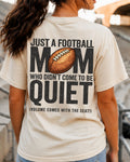Football mom game day shirt worn in stadium stands on an ivory Comfort Colors tee with back design reading “Just a football mom who didn’t come to be quiet volume comes with the seat”