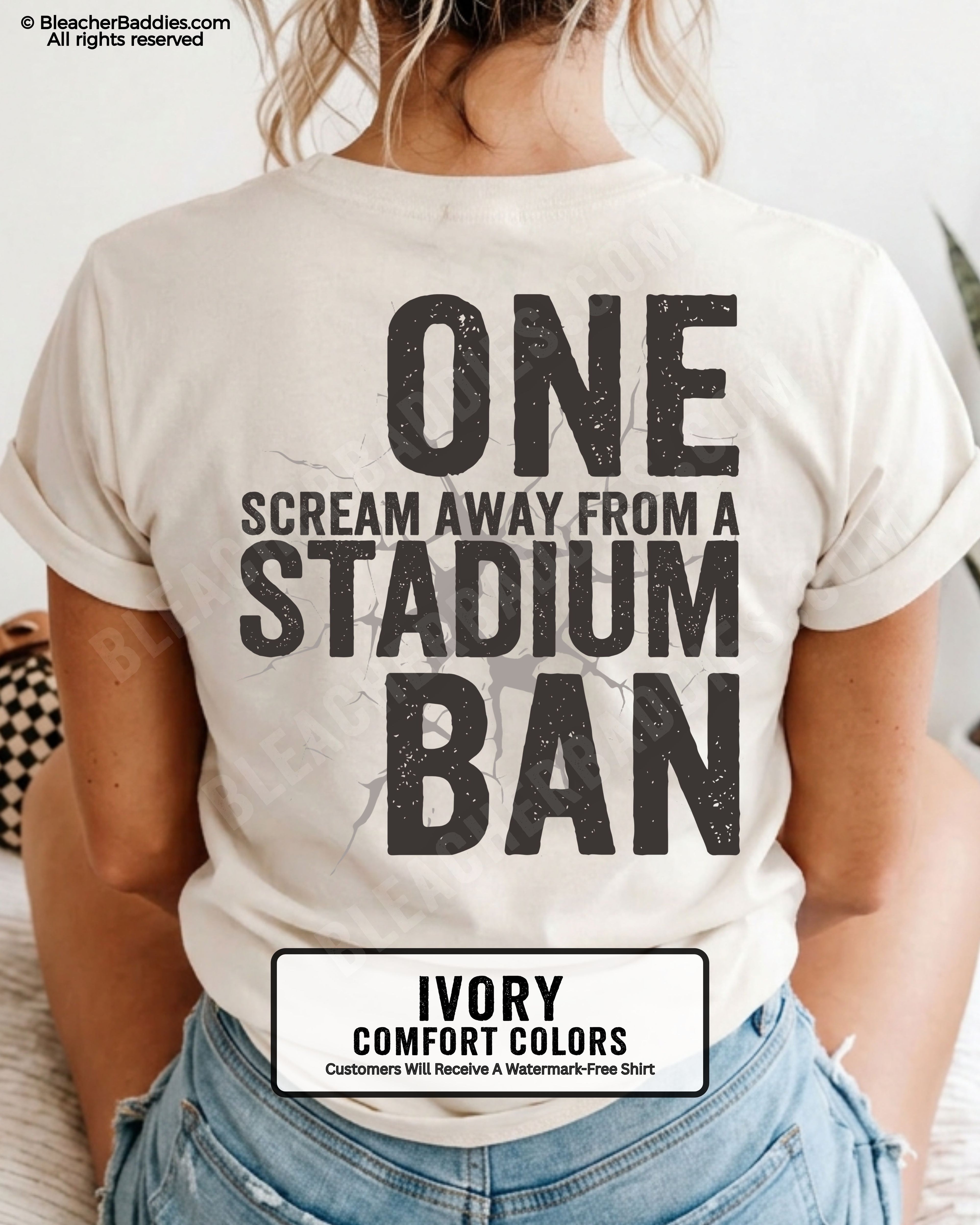 Woman wearing an ivory t-shirt with a large distressed black back graphic that reads “One Scream Away From a Stadium Ban” with a cracked texture effect across the design.