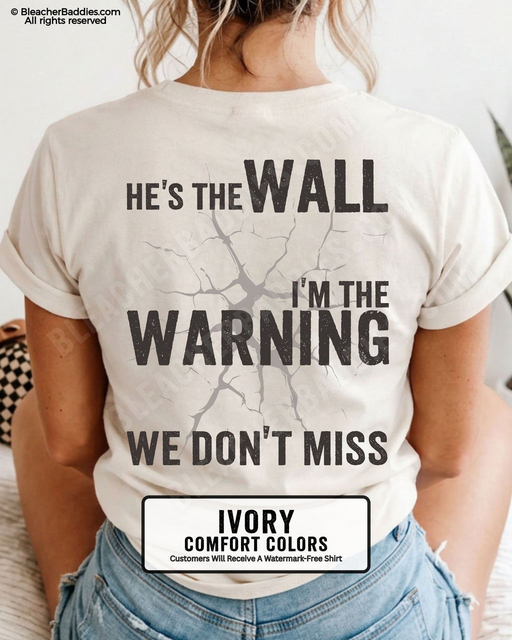 Woman wearing an ivory football mom game day shirt shown from the back featuring a large distressed black graphic that reads “He’s the Wall I’m the Warning We Don’t Miss.”
