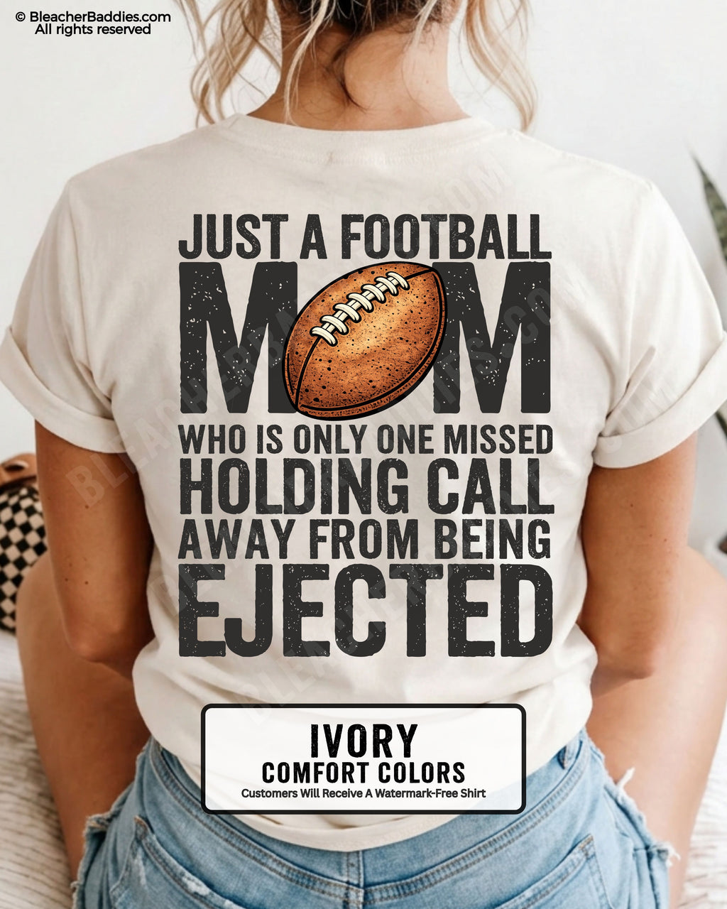 Back view of a woman wearing an ivory Comfort Colors football mom shirt, displaying bold distressed text that reads “Just a football mom who is only one missed holding call away from being ejected,” with a football graphic on the back.