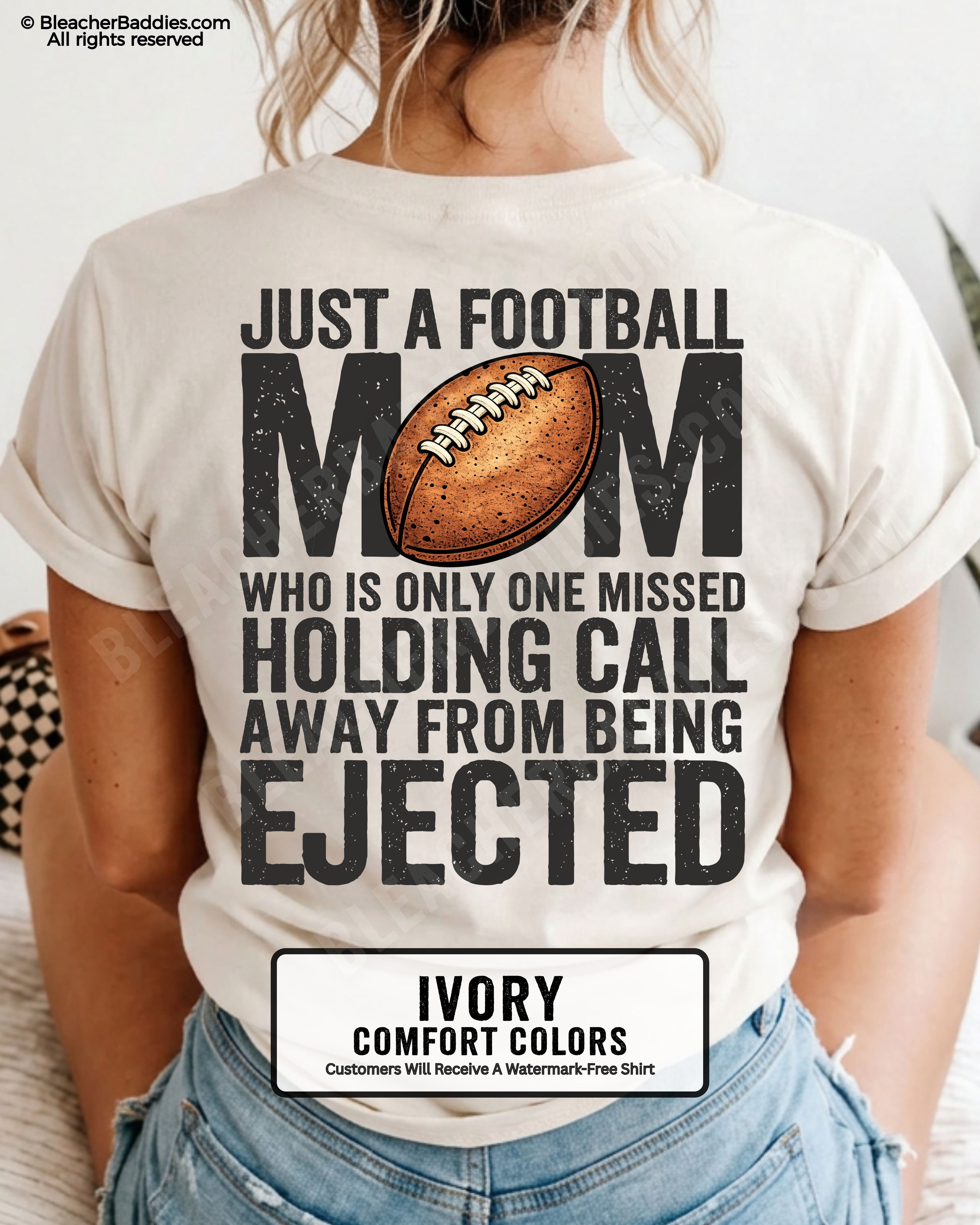 Back view of a woman wearing an ivory Comfort Colors football mom shirt, displaying bold distressed text that reads “Just a football mom who is only one missed holding call away from being ejected,” with a football graphic on the back.