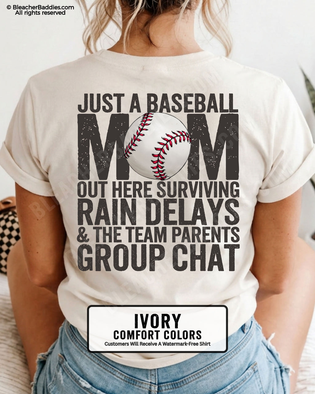 Ivory baseball mom graphic tee featuring distressed black back design reading “Just a baseball mom out here surviving rain delays and the team parents group chat” with baseball illustration centered in MOM