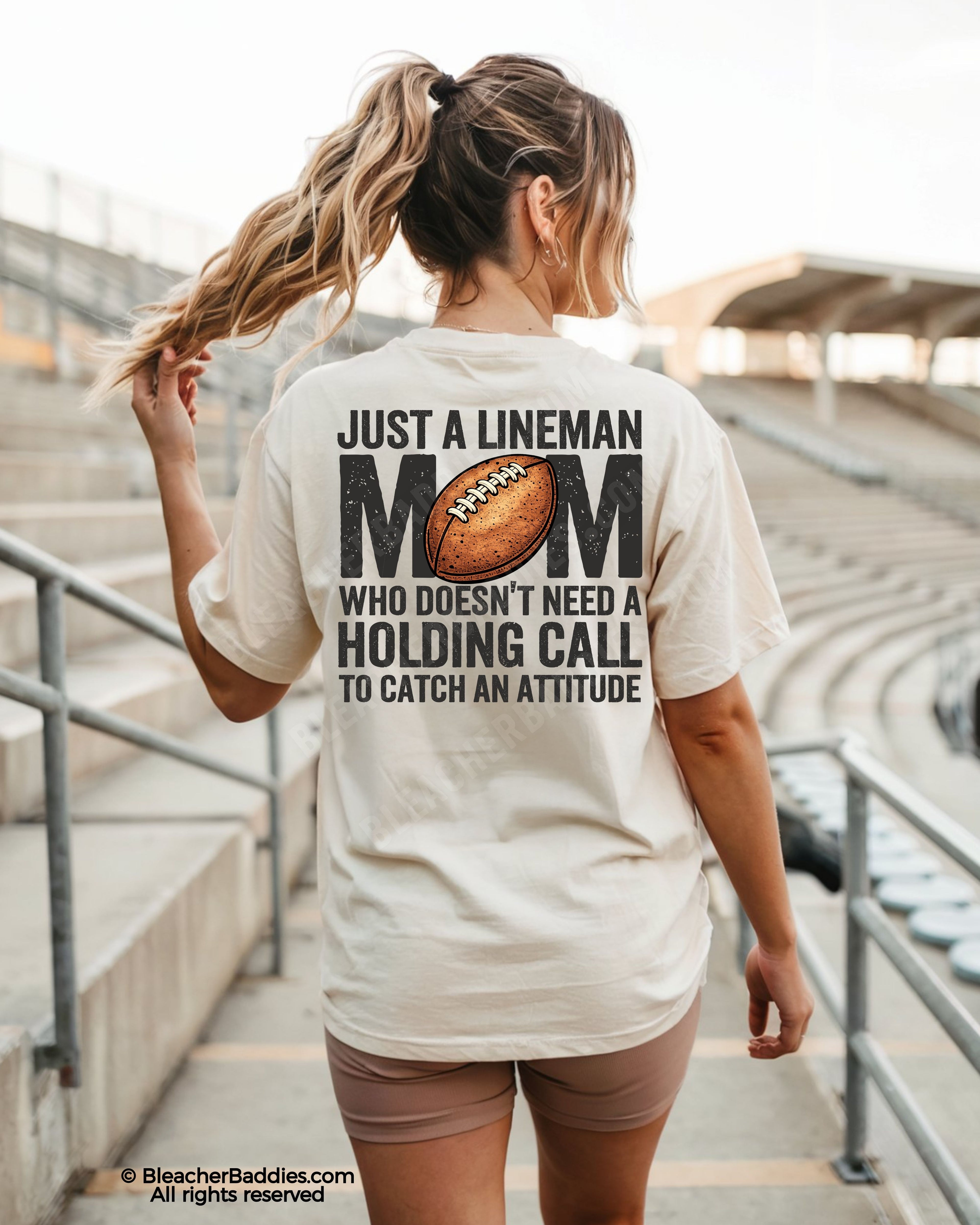Woman wearing ivory Comfort Colors lineman mom football game day shirt with back print that says “Just a lineman mom who doesn’t need a holding call to catch an attitude”