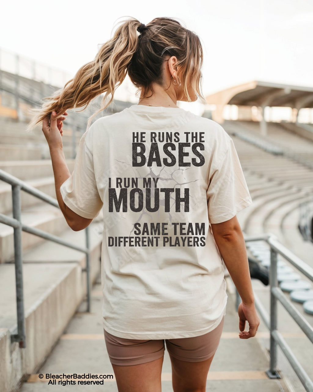 Woman wearing ivory Comfort Colors baseball mom shirt at stadium featuring bold distressed back graphic that says “He Runs The Bases I Run My Mouth” with “Same Team Different Players” across the back