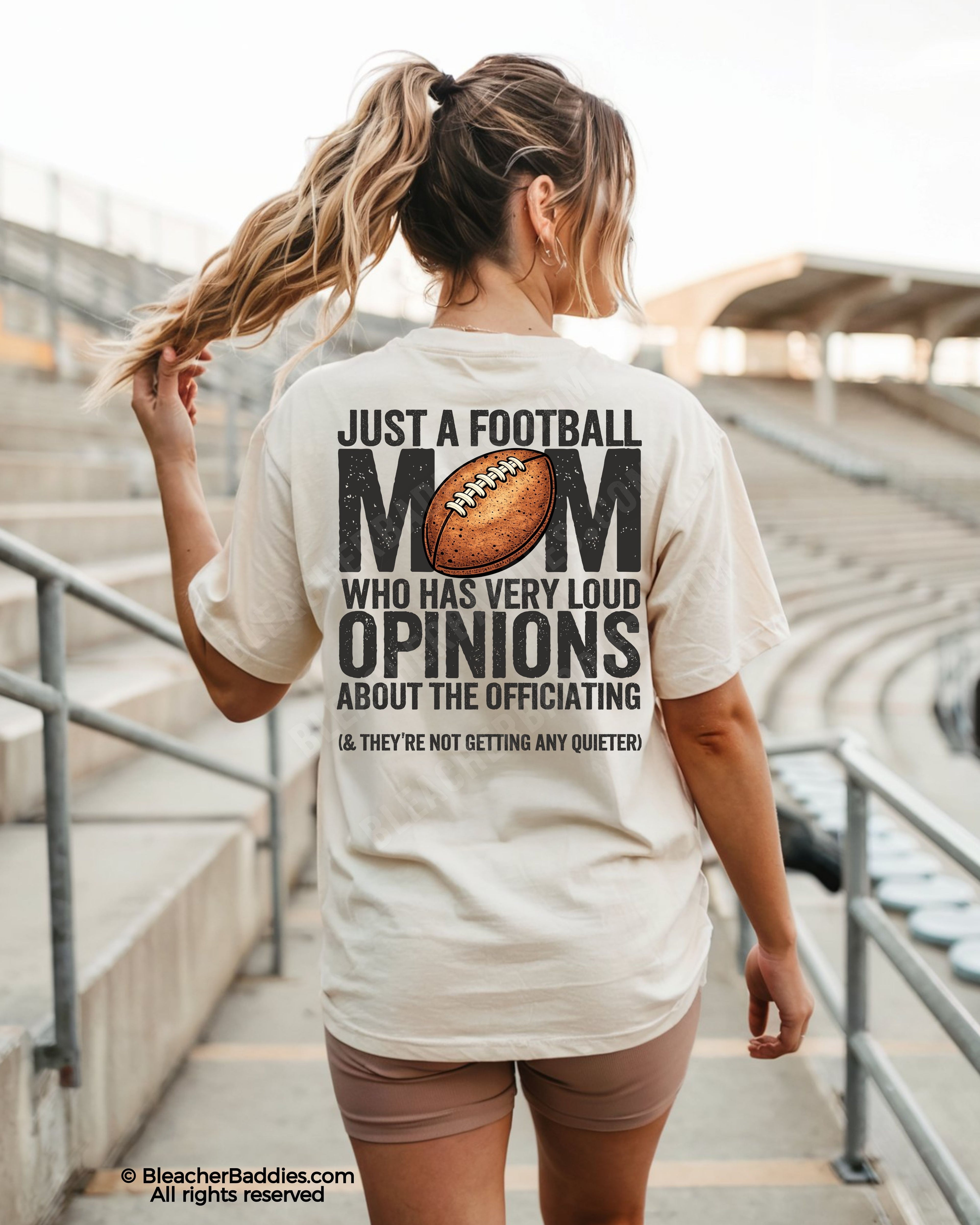 Football mom game day shirt worn by a model in a stadium, shown on a Comfort Colors tee with a back graphic that says, “Just a football mom who has very loud opinions about the officiating (& they’re not getting any quieter).”