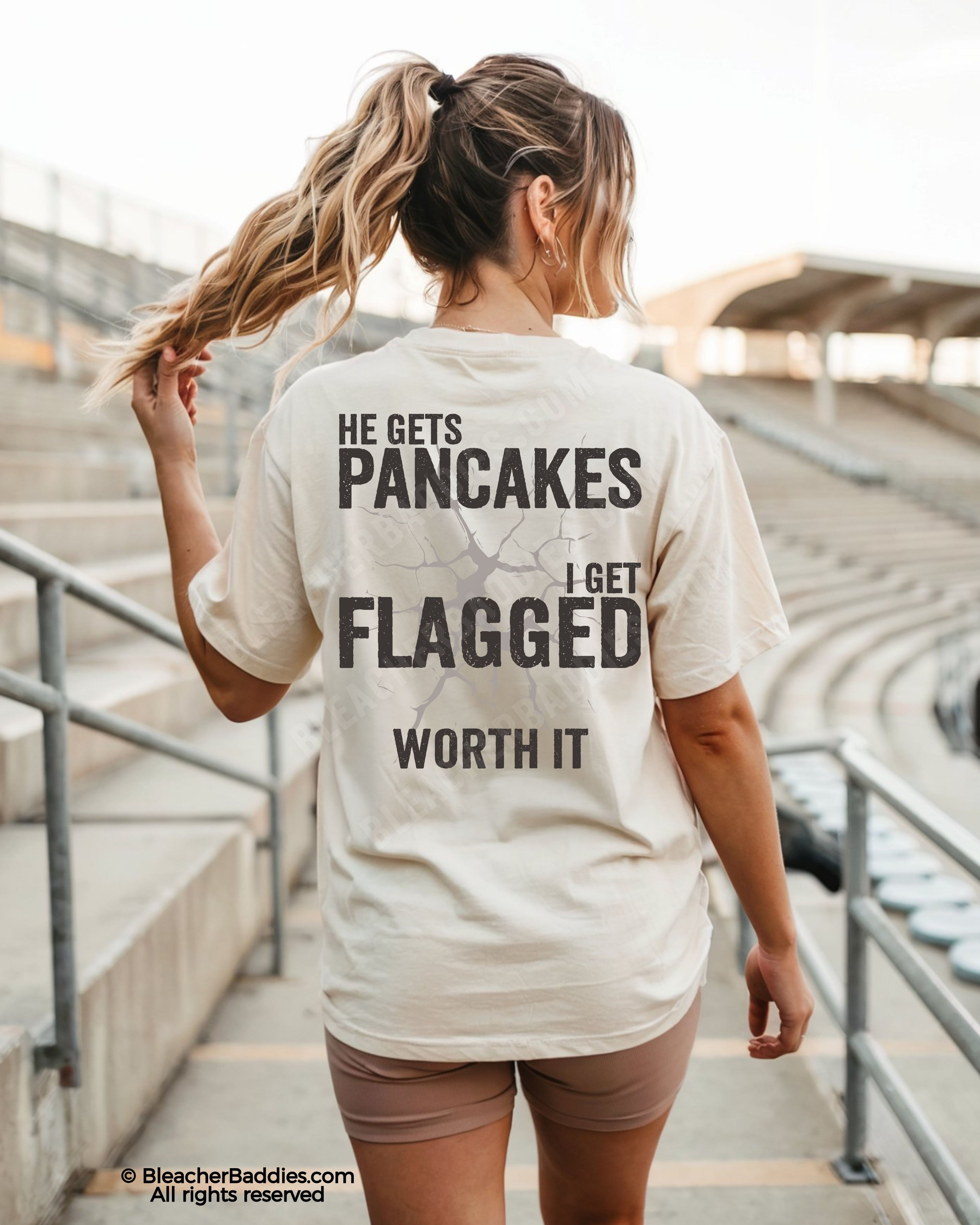 Football mom game day shirt worn in stadium with back design that reads “He gets pancakes I get flagged worth it” in distressed black text with cracked graphic
