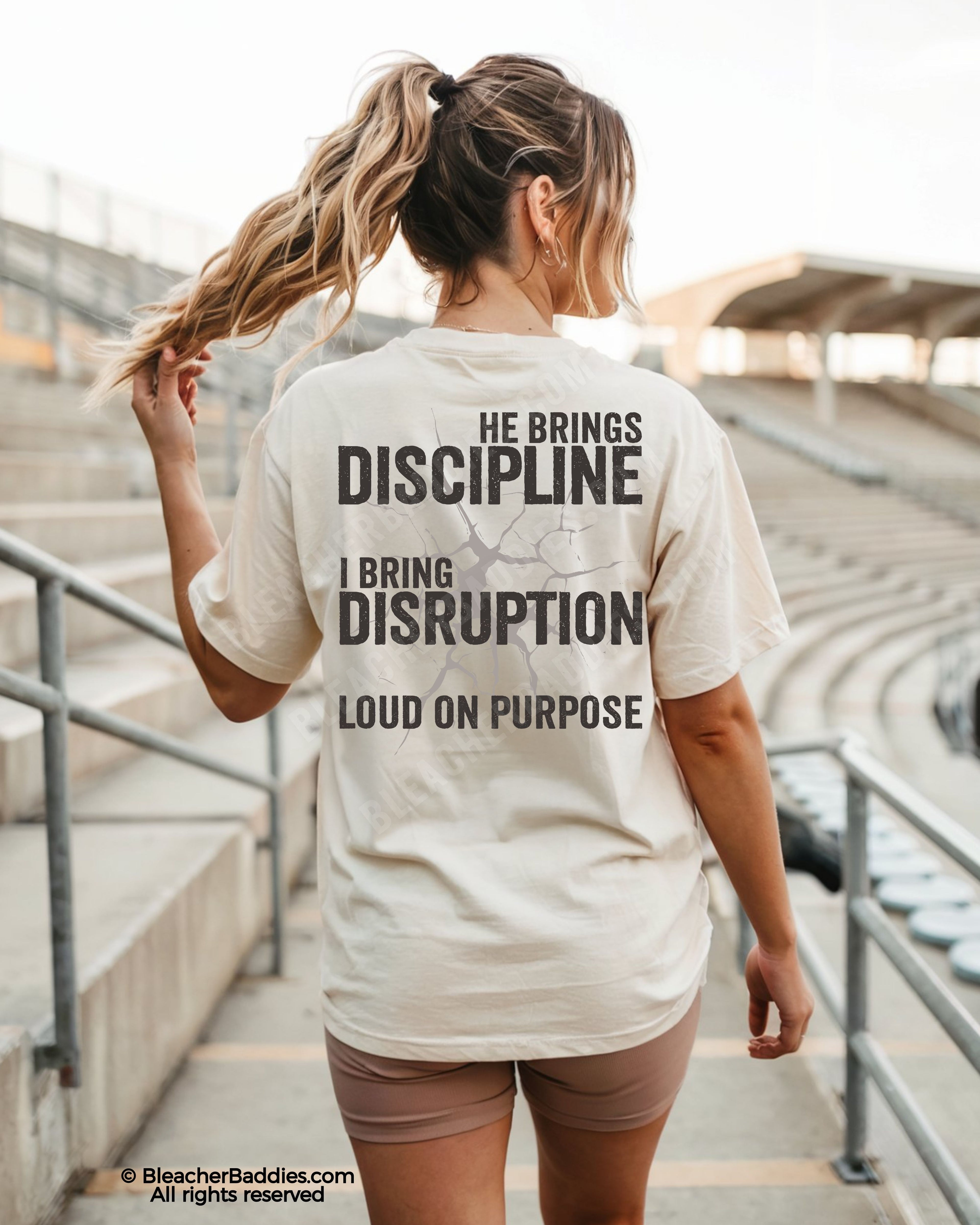 Woman wearing ivory Comfort Colors game day shirt at a baseball stadium featuring oversized distressed “He Brings Discipline I Bring Disruption” back print with “Loud On Purpose” text.