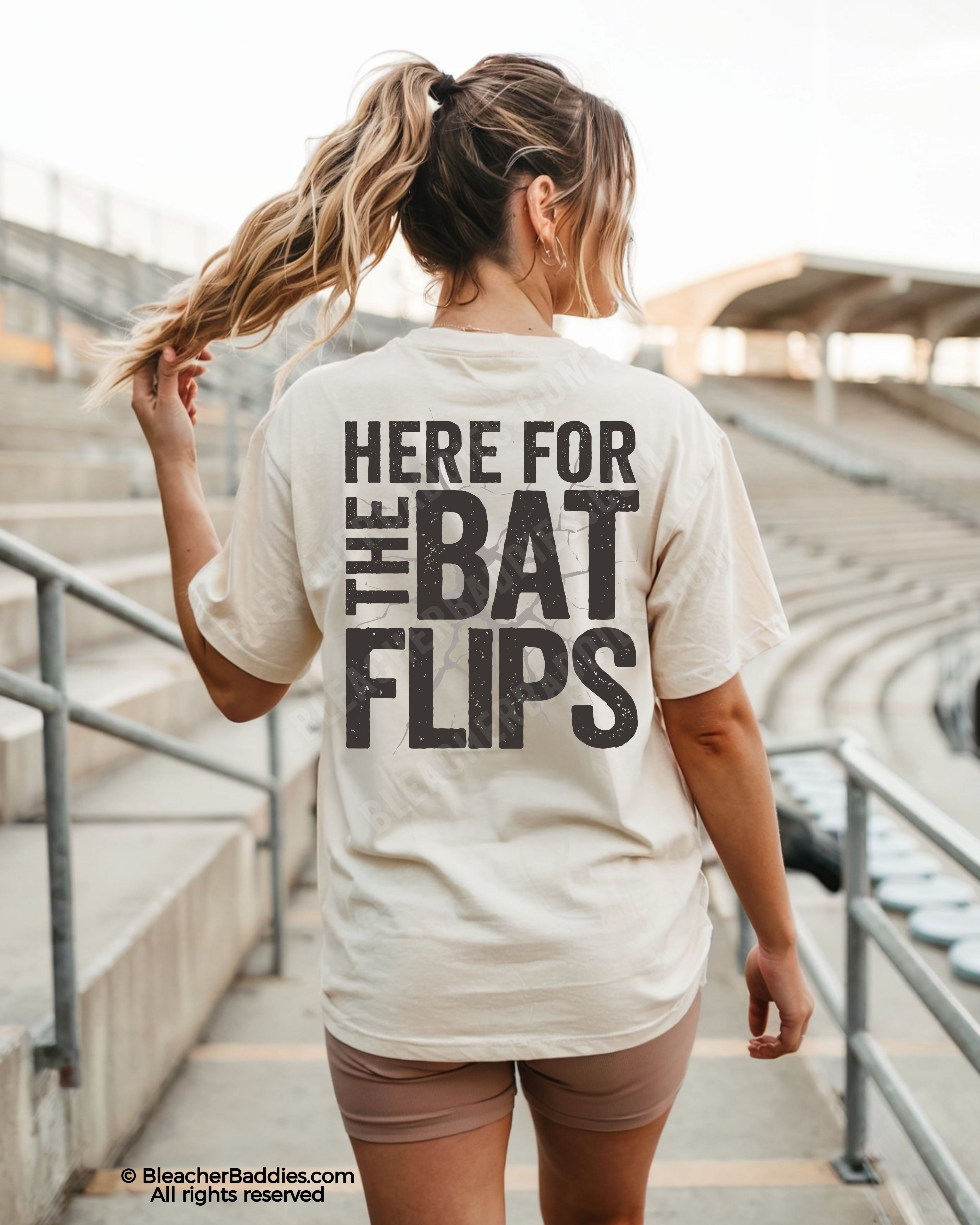 Woman wearing ivory Comfort Colors baseball mom shirt at stadium featuring bold distressed back graphic that says “Here For The Bat Flips”
