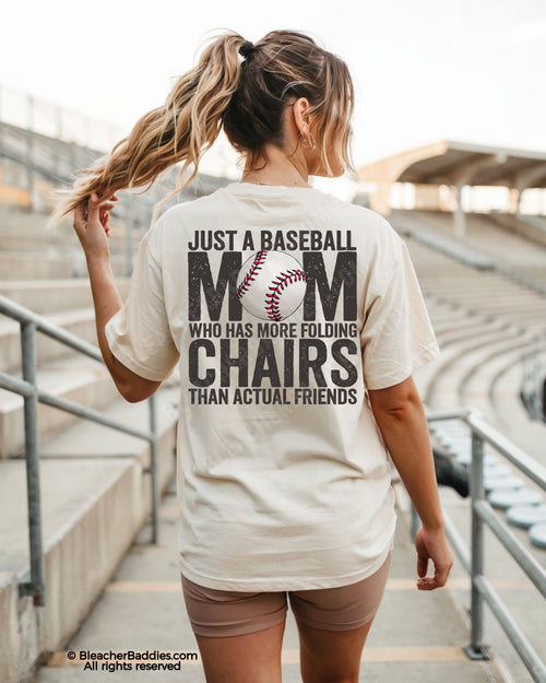 Woman wearing ivory Comfort Colors baseball mom shirt in stadium with oversized distressed back graphic reading “Just a baseball mom who has more folding chairs than actual friends”