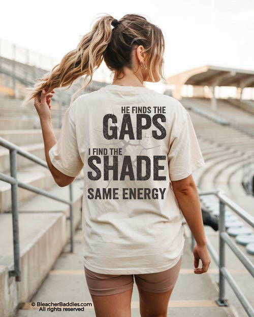 Woman wearing ivory Comfort Colors baseball mom shirt at stadium featuring bold distressed back graphic that says “He Finds The Gaps I Find The Shade Same Energy”