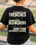 Woman wearing black comfort colors t-shirt in stadium showing back graphic that reads “He Dominates the Trenches I Dominate the Bleachers Same Team Different Players” Lineman mom shirt Offensive Lineman Shirt. Football Mom shirt.