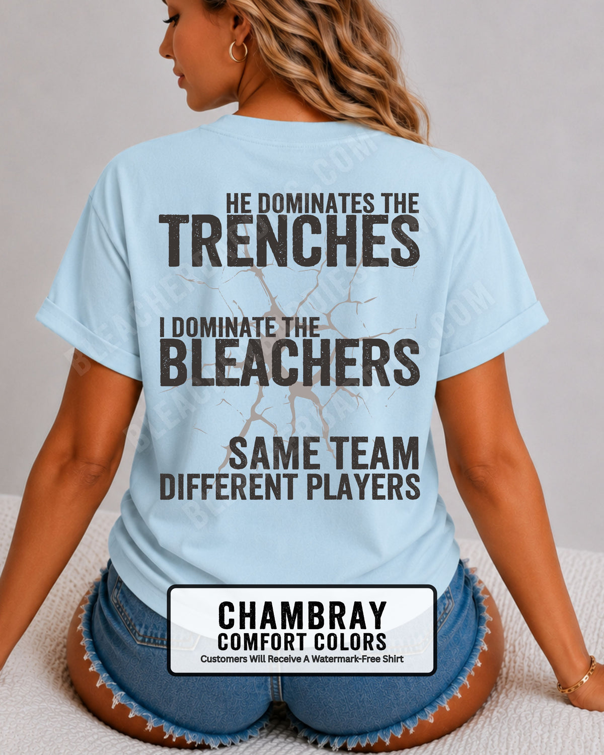 Close-up of woman wearing chambray blue comfort colors t-shirt back print with distressed text “He Dominates the Trenches I Dominate the Bleachers Same Team Different Players” and cracked design detail