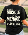 Woman wearing black Comfort Colors football mom game day shirt in stadium with back design that reads “He’s the muscle I’m the menace we don’t miss” in distressed cream text with cracked graphic.  Football mom shirt. Lineman mom shirt.