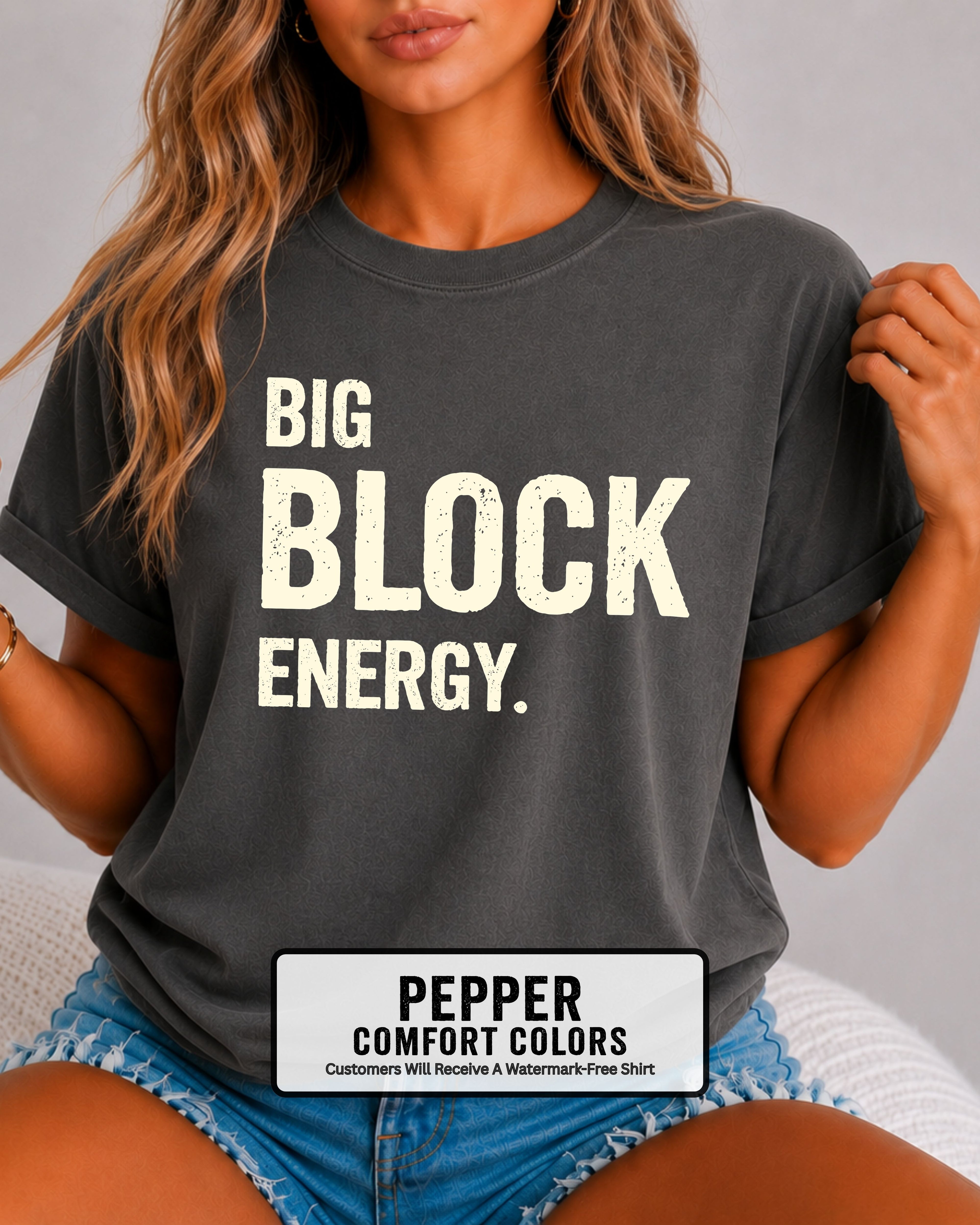 woman wearing a pepper Comfort Colors t-shirt featuring the phrase "Big Block Energy" in distressed cream lettering. She is seated in light blue patterned shorts, making this the perfect football game day shirt for football moms, offensive line moms, lineman girlfriends, wives, and fans who love the big guys in the trenches.