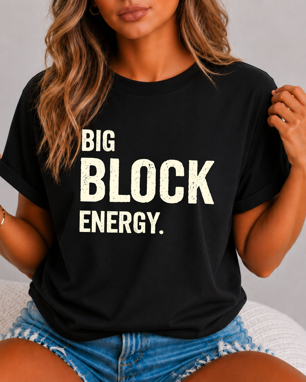 woman wearing a black Comfort Colors t-shirt featuring the phrase "Big Block Energy" in distressed cream lettering. She is seated in light blue patterned shorts, making this the perfect football game day shirt for football moms, offensive line moms, lineman girlfriends, wives, and fans who love the big guys in the trenches.