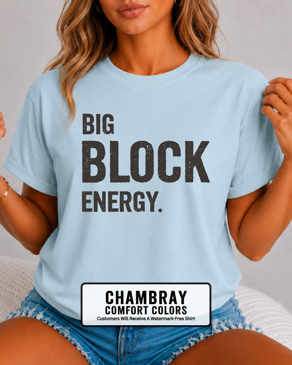 woman wearing a chambray blue Comfort Colors t-shirt featuring the phrase "Big Block Energy" in distressed dark lettering. She is seated in light blue patterned shorts, making this the perfect football game day shirt for football moms, offensive line moms, lineman girlfriends, wives, and fans who love the big guys in the trenches.