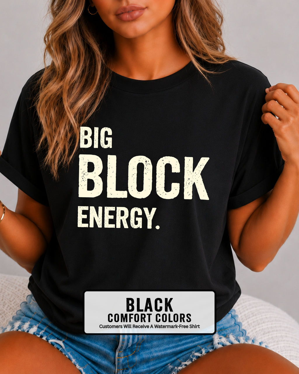 woman wearing a black Comfort Colors t-shirt featuring the phrase "Big Block Energy" in distressed cream lettering. She is seated in light blue patterned shorts, making this the perfect football game day shirt for football moms, offensive line moms, lineman girlfriends, wives, and fans who love the big guys in the trenches.