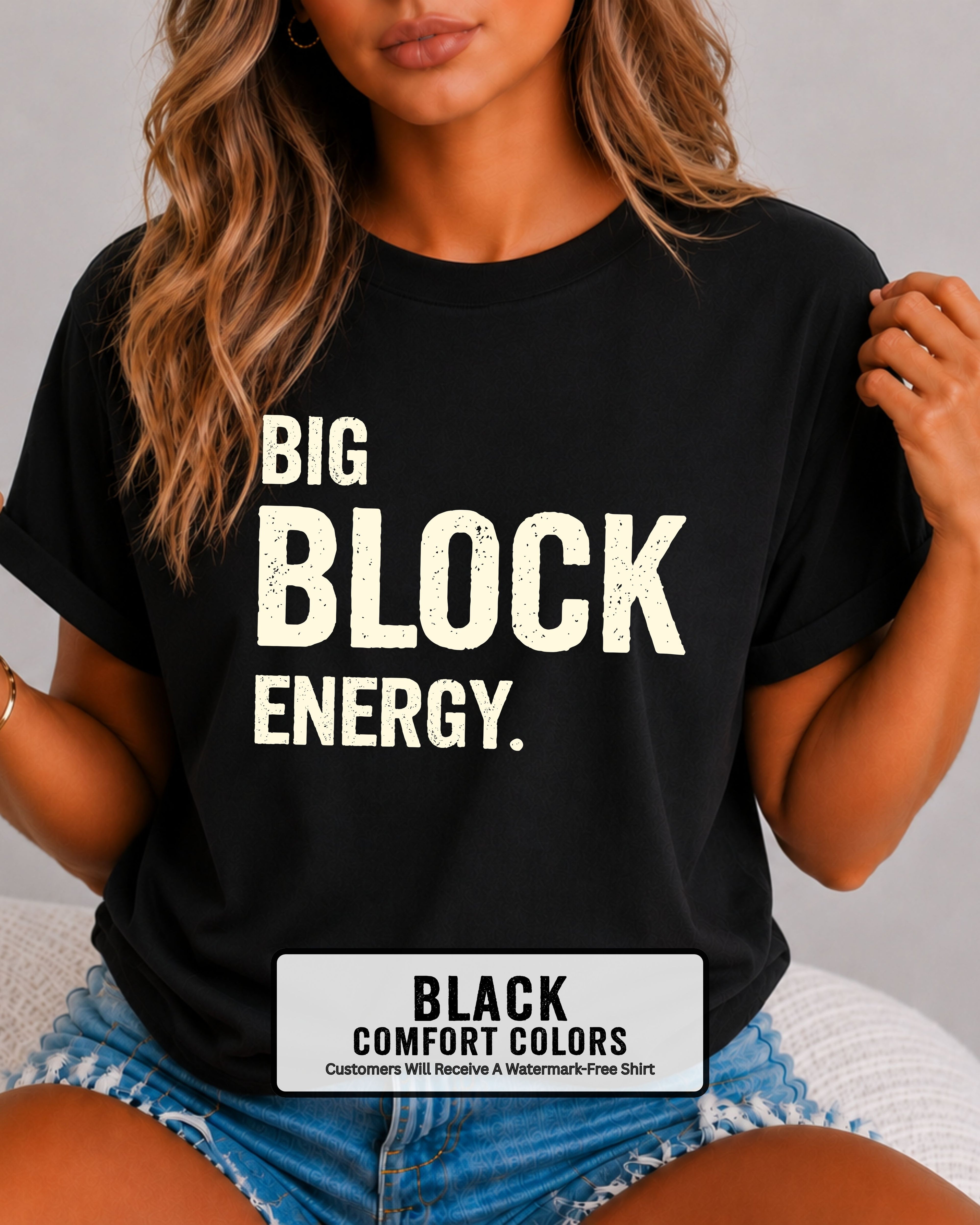 woman wearing a black Comfort Colors t-shirt featuring the phrase "Big Block Energy" in distressed cream lettering. She is seated in light blue patterned shorts, making this the perfect football game day shirt for football moms, offensive line moms, lineman girlfriends, wives, and fans who love the big guys in the trenches.