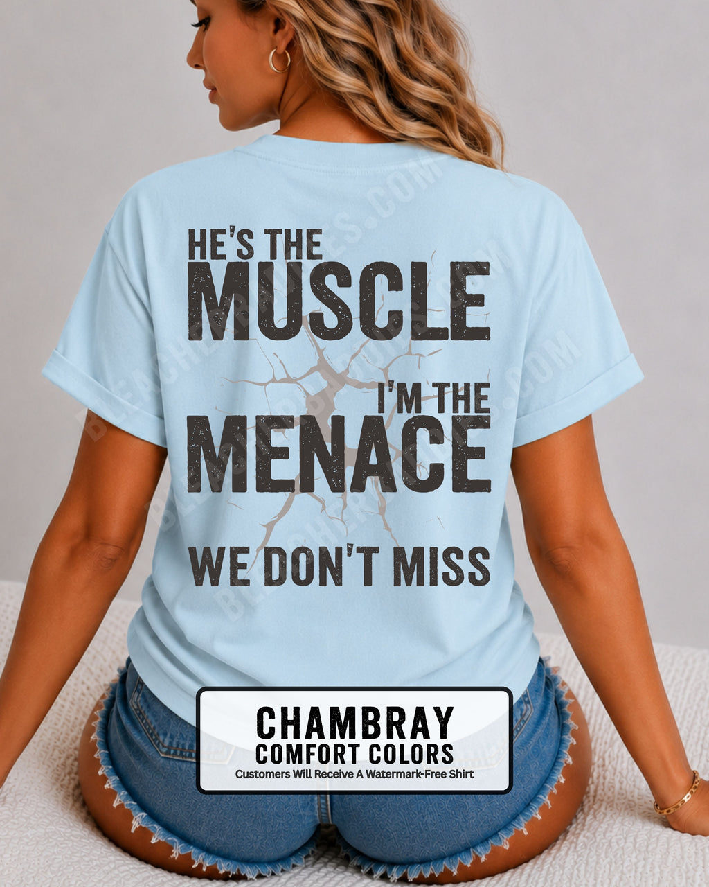 Woman wearing chambray blue Comfort Colors football mom game day shirt with back design that reads “He’s the muscle I’m the menace we don’t miss” in distressed black text with cracked graphic.  Football mom shirt.  Lineman mom shirt.