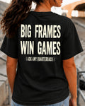 Back view of a woman standing in football stadium bleachers wearing a black Comfort Colors t-shirt with the bold distressed phrase, "BIG FRAMES WIN GAMES (ASK ANY QUARTERBACK)." A relaxed ponytail and blurred stadium background create the perfect game day look for football fans, offensive line parents, and linemen.