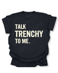 Flat lay of a black Comfort Colors t-shirt featuring the distressed ivory text "TALK TRENCHY TO ME." in large block letters. The shirt is displayed on a white background with rolled sleeves, showcasing a bold football offensive line-inspired graphic perfect for linemen, football players, coaches, and trench football fans.